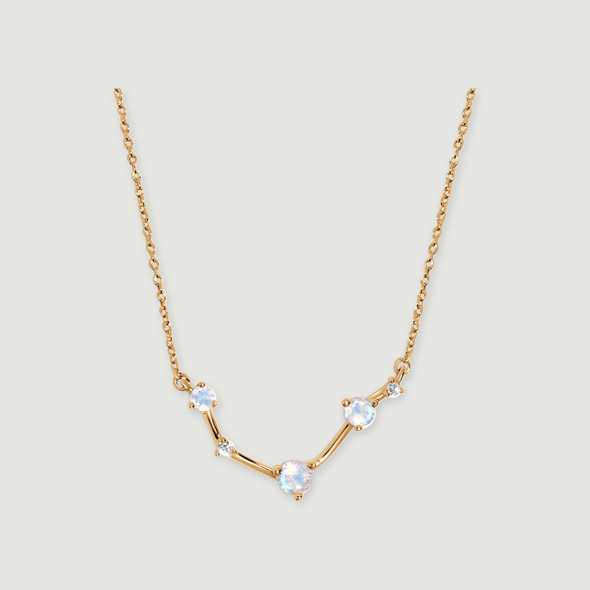 A yellow gold necklace with three round iridescent stones and two small clear stones rests on a light grey surface.