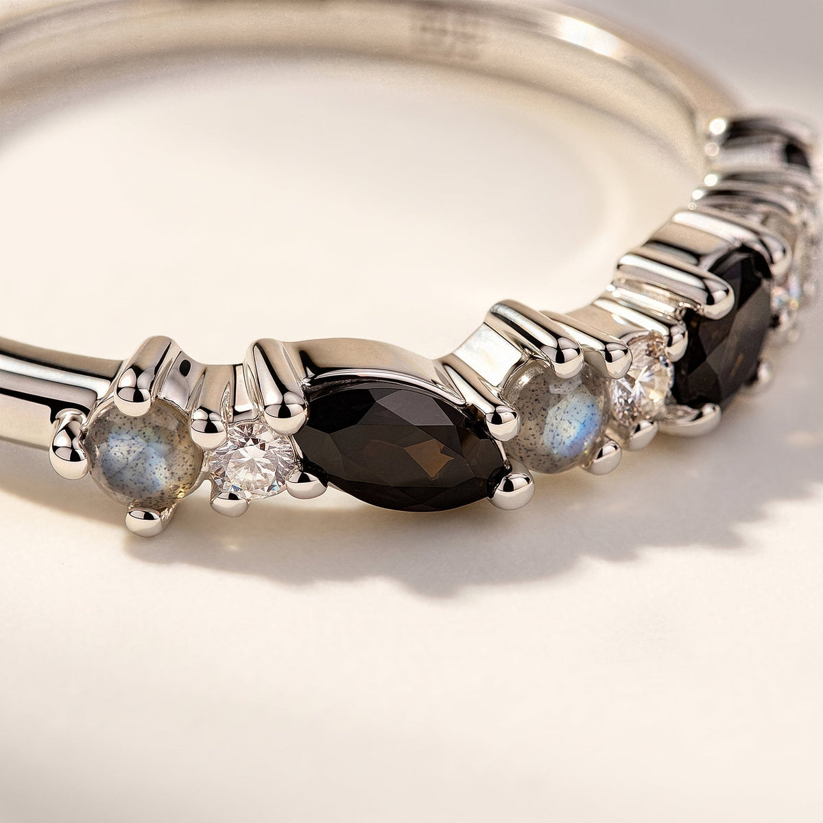 Polished silver prongs hold a dark faceted marquise stone beside clear and blue gray round stones.