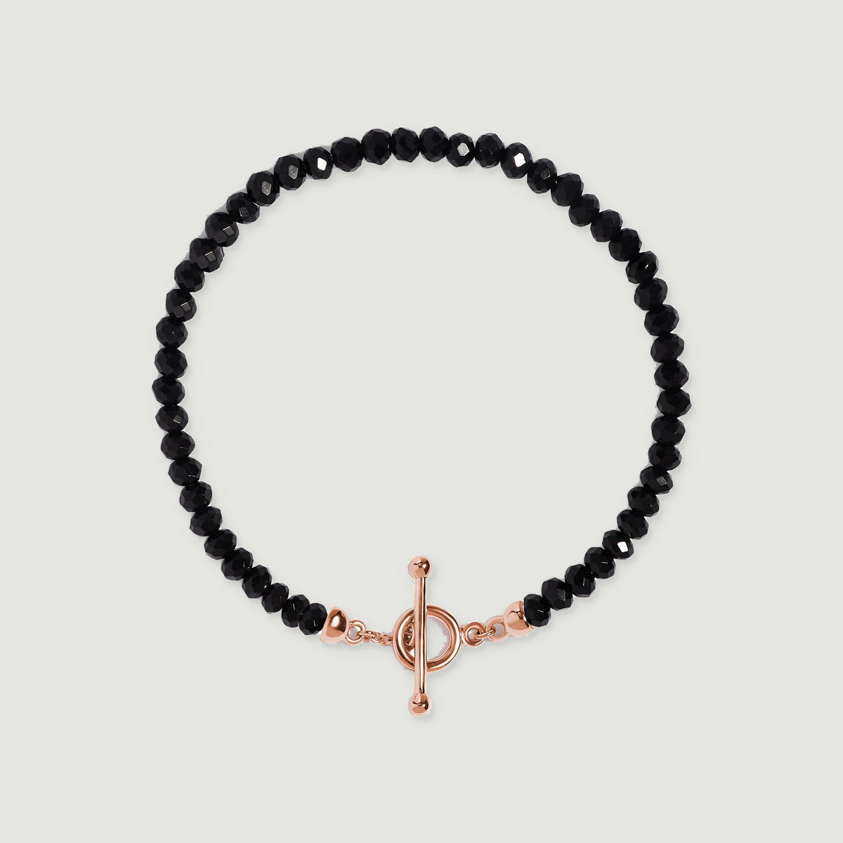 A black obsidian bead bracelet lies centered on light gray with a rose gold vermeil ring and slender bar closure.