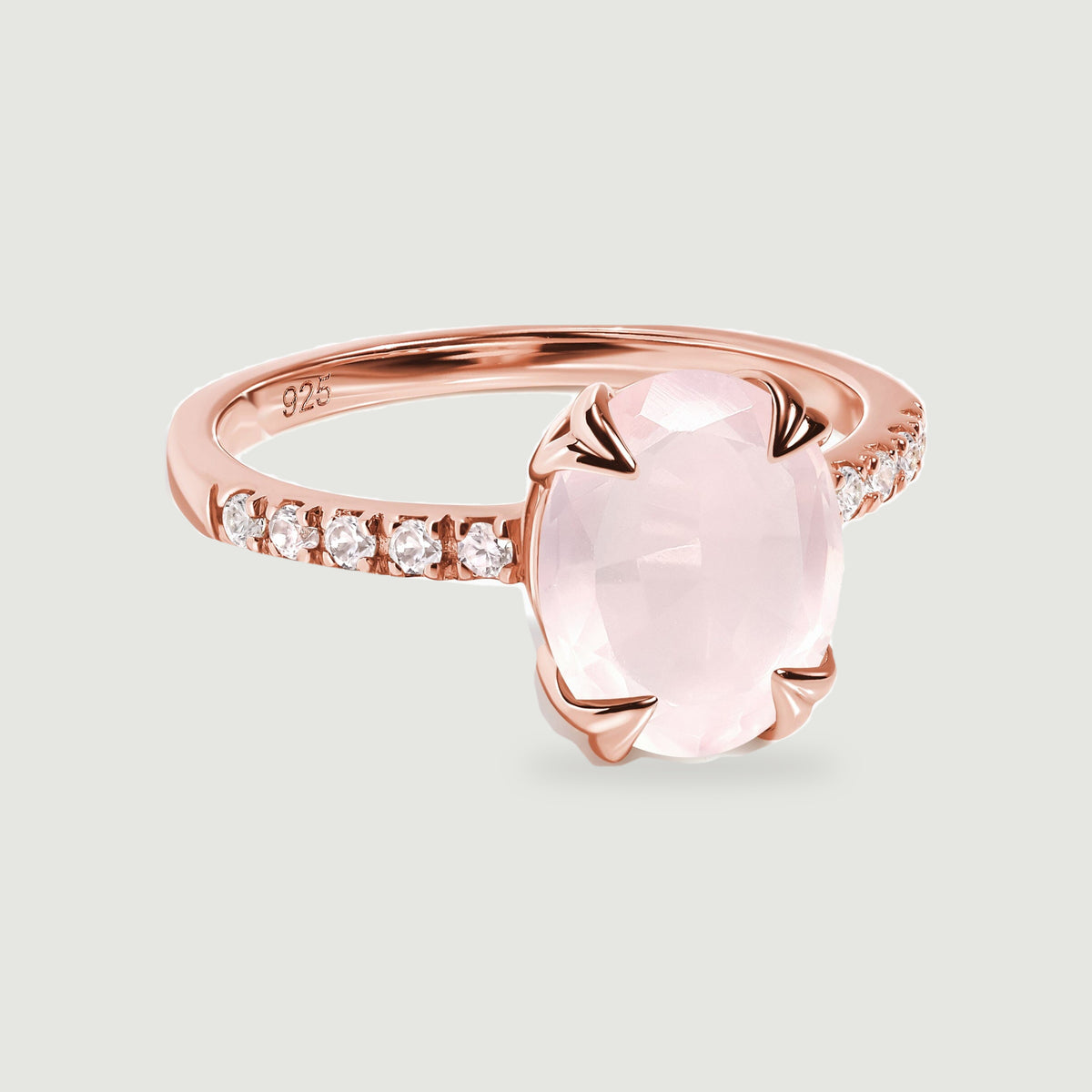 A rose gold vermeil ring with clear stones along its shoulders is centered on a soft gray background.