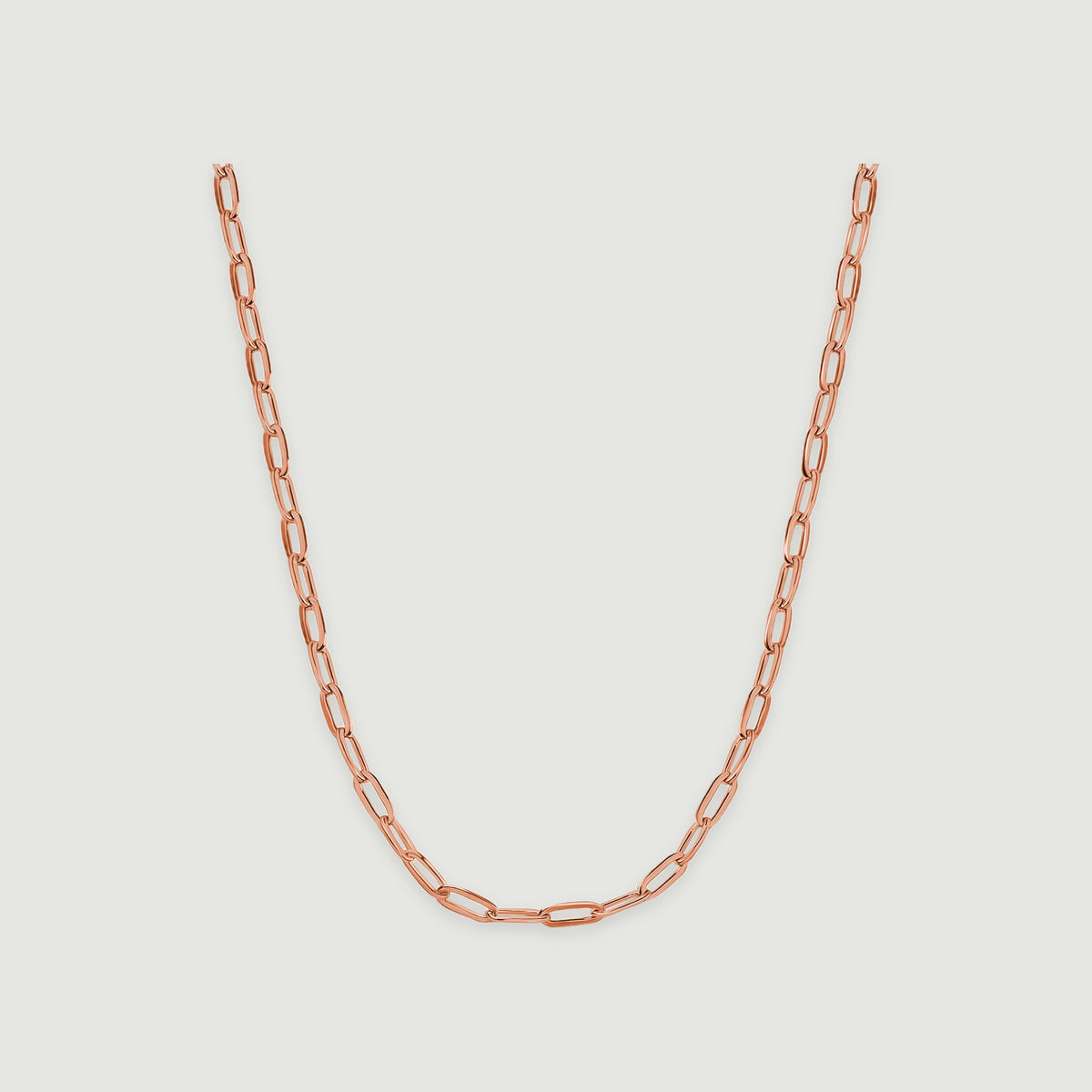 A rose gold necklace curves downward with polished rectangular links against a pale gray surface.