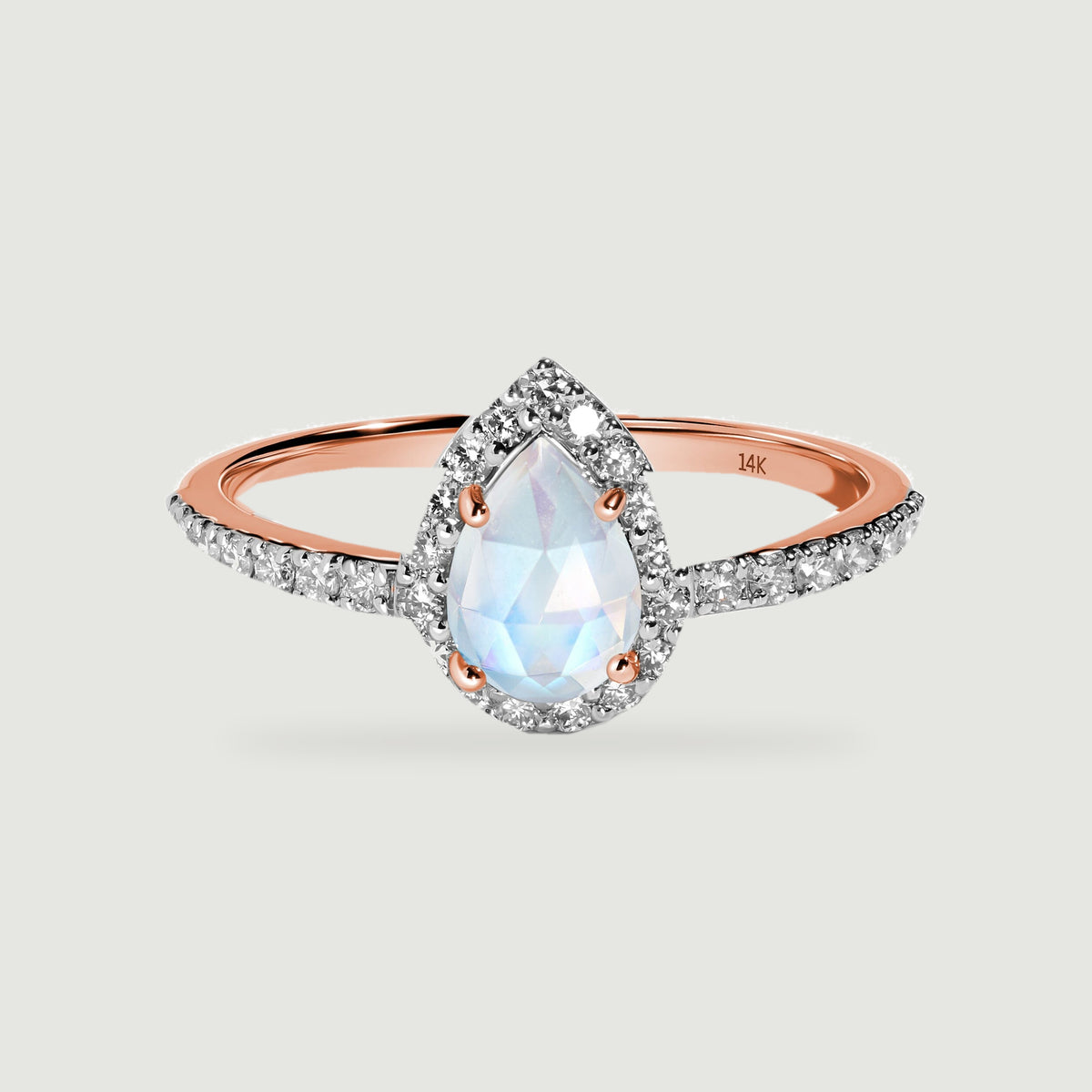 A rose gold band holds a pale pear-shaped moonstone surrounded by a bright diamond halo.