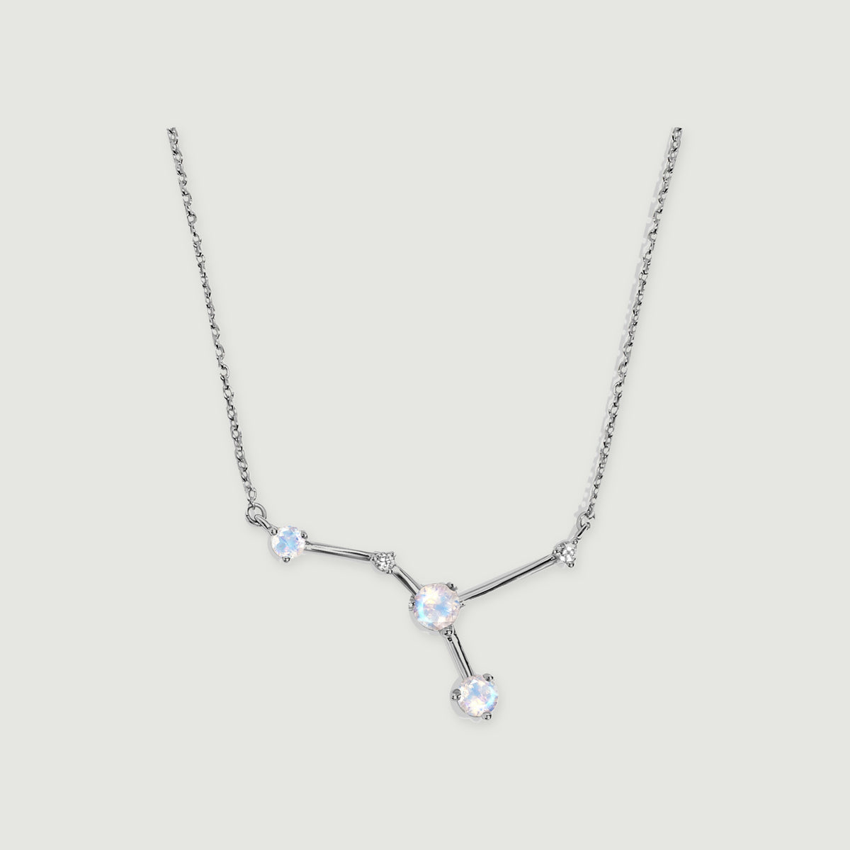 A silver necklace displays three round moonstones and two smaller clear stones joined by polished bars on a light grey background.