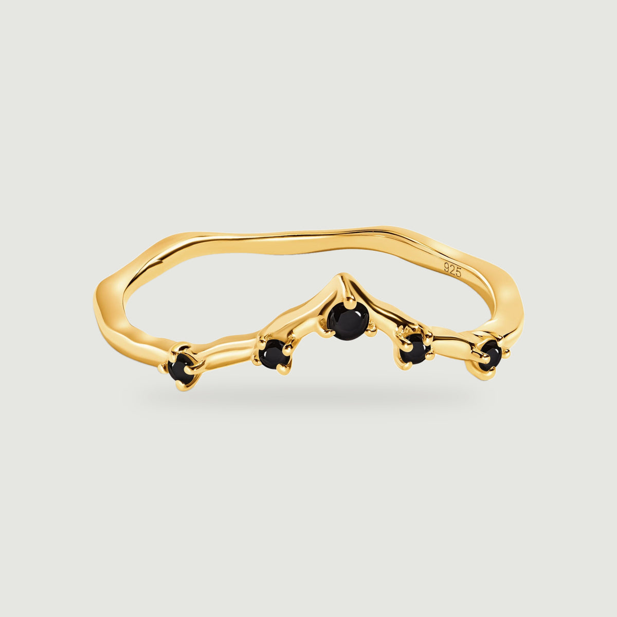 A yellow gold ring with five round black stones rests on a light gray background.