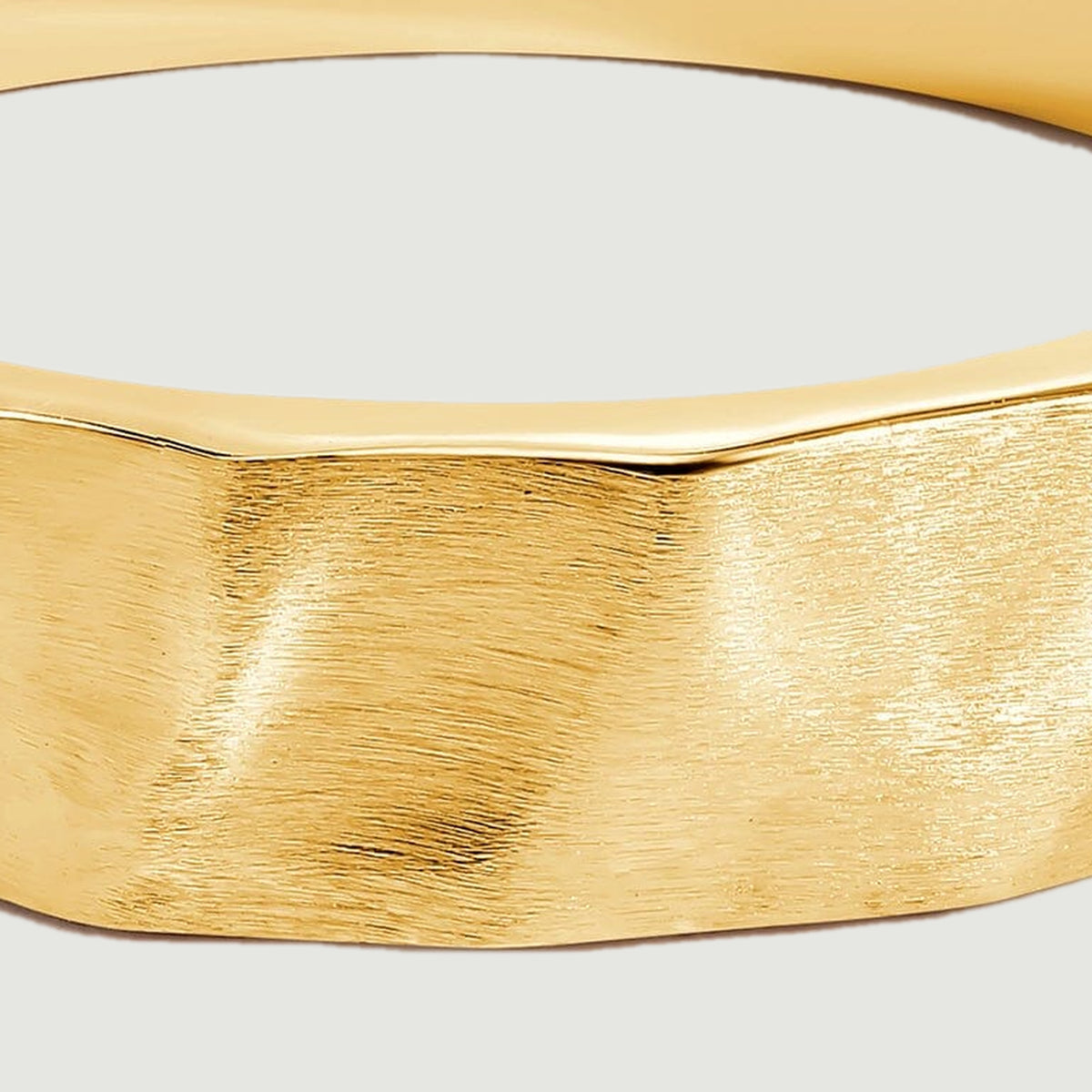 A close view shows the brushed grain and shallow facets across the yellow gold band.