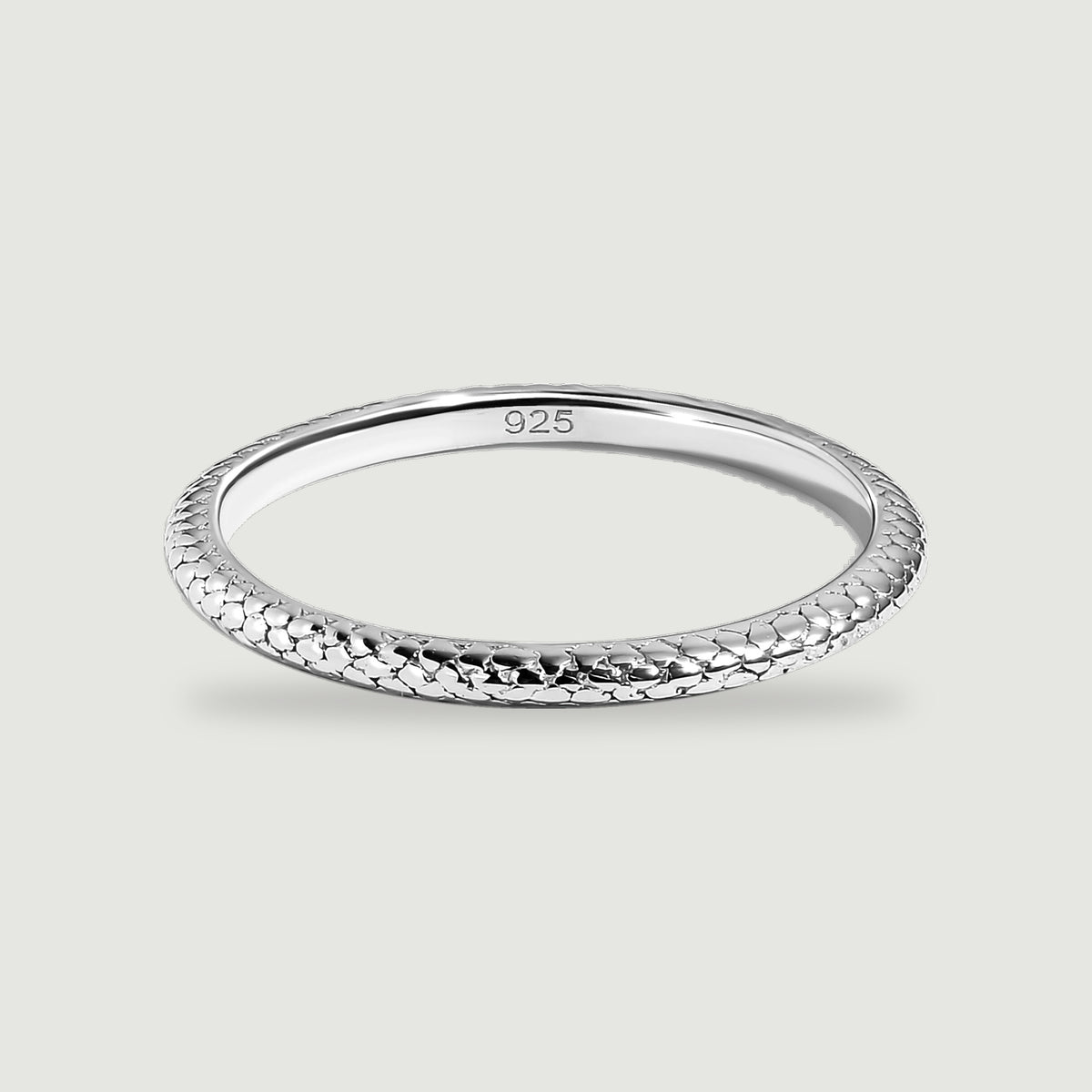A polished silver ring with a scale-textured band rests on a light gray surface.