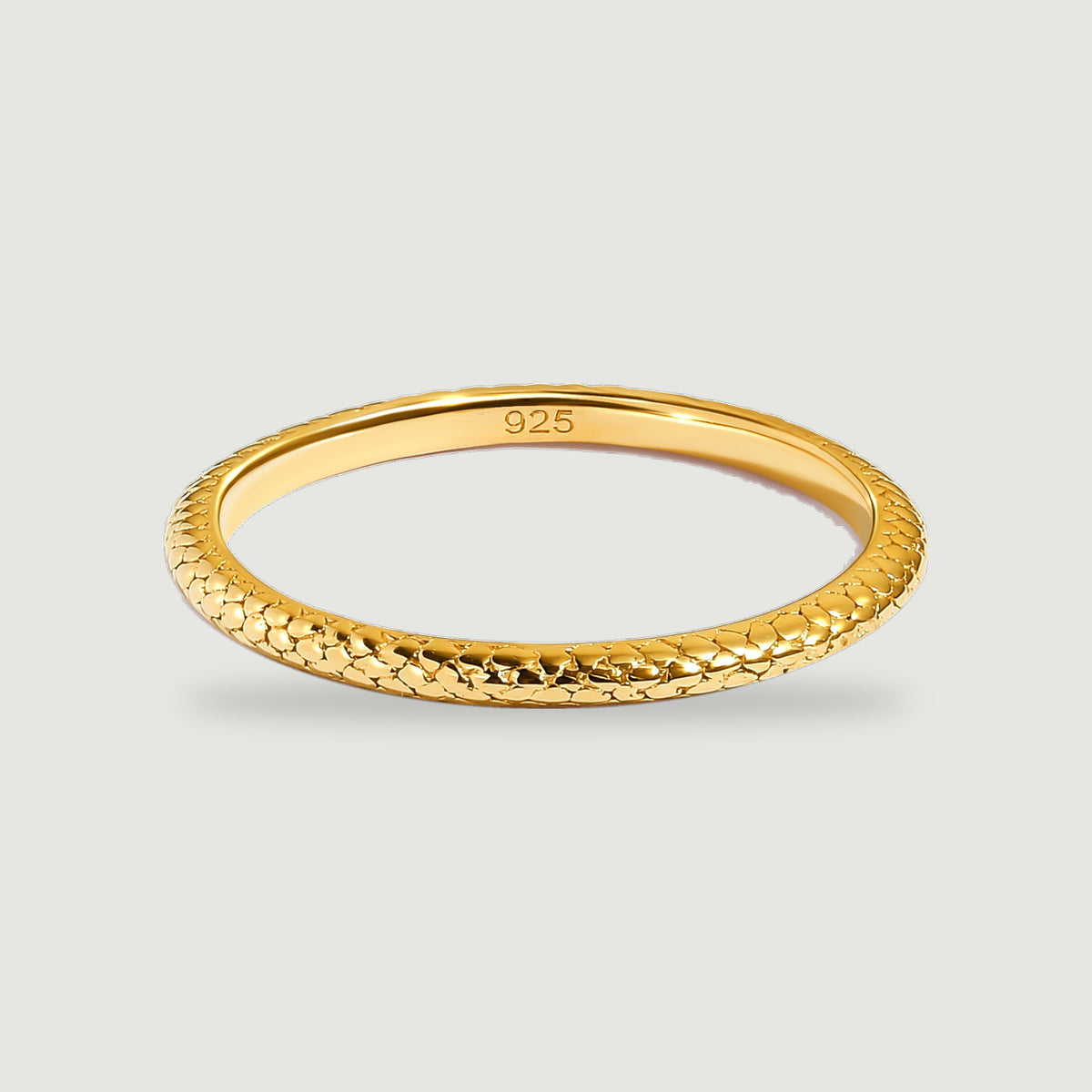 A yellow gold ring shows a textured outer band and a smooth inner surface against light gray.