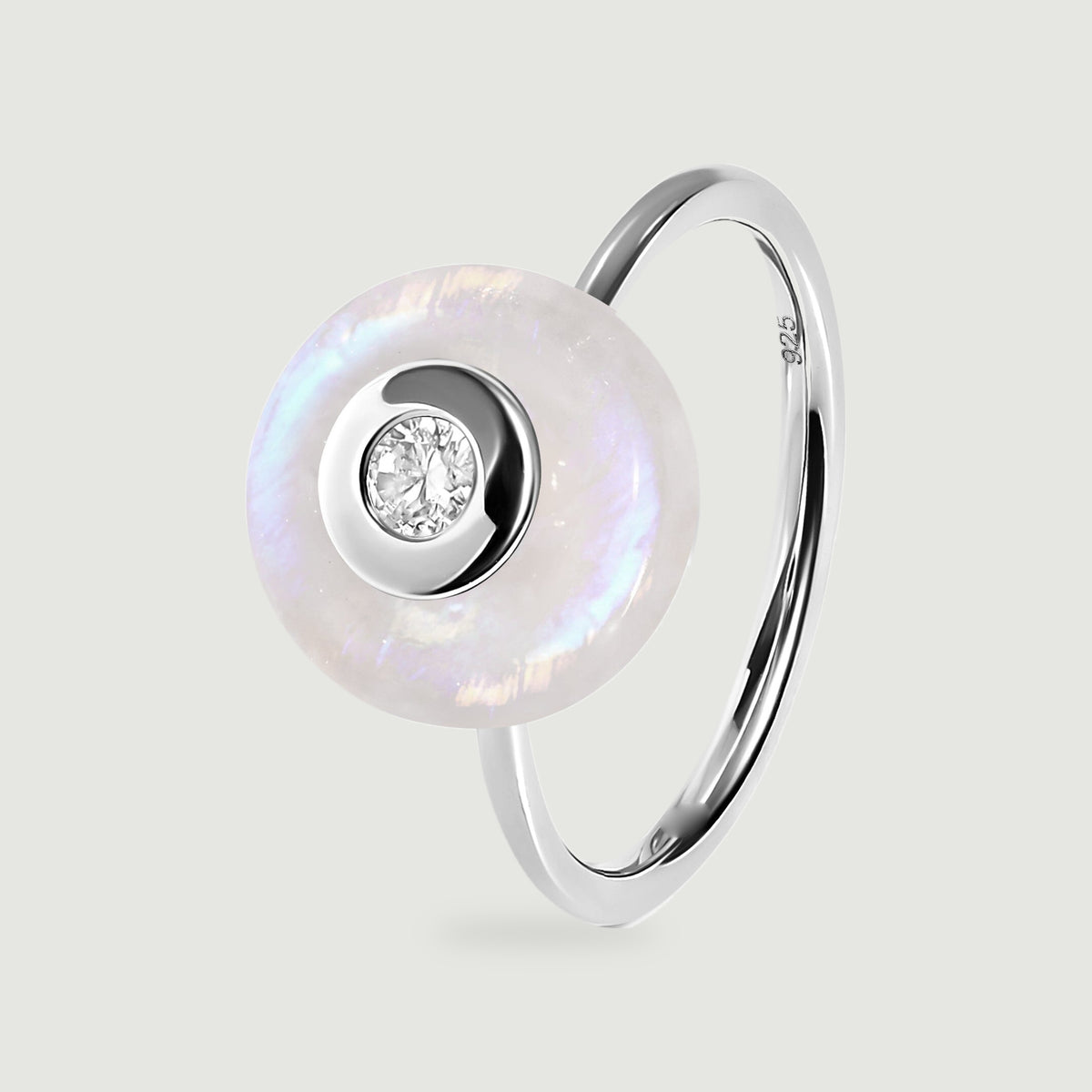 A sterling silver ring stands at an angle with a pale moonstone disc, a clear center stone, and a slim polished band.