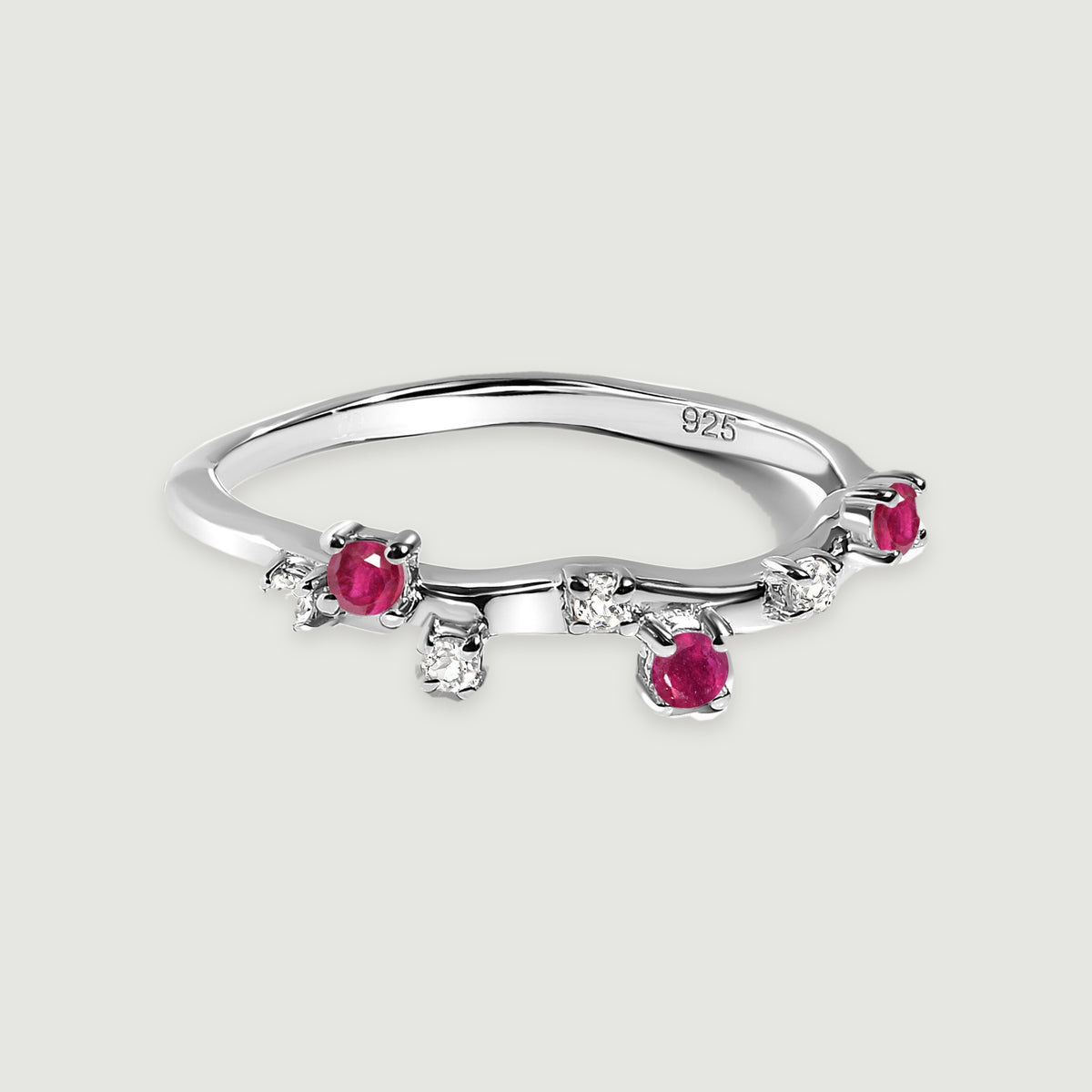 A sterling silver ring with round pink-red and clear stones rests on a light grey surface.