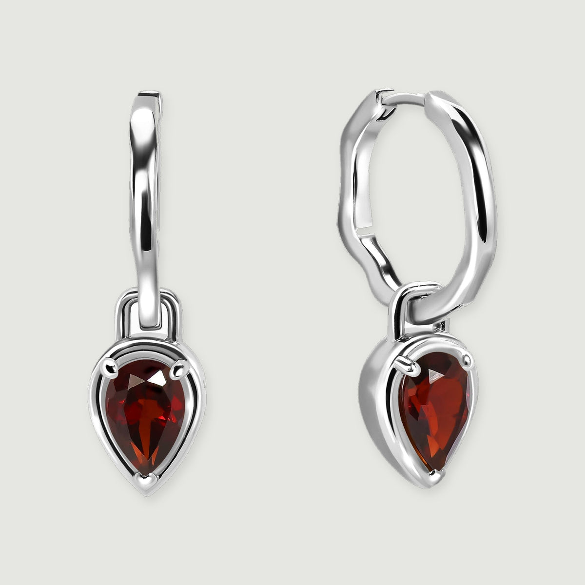 A pair of silver-tone hoops with red teardrop garnets is centered over a soft contact shadow.