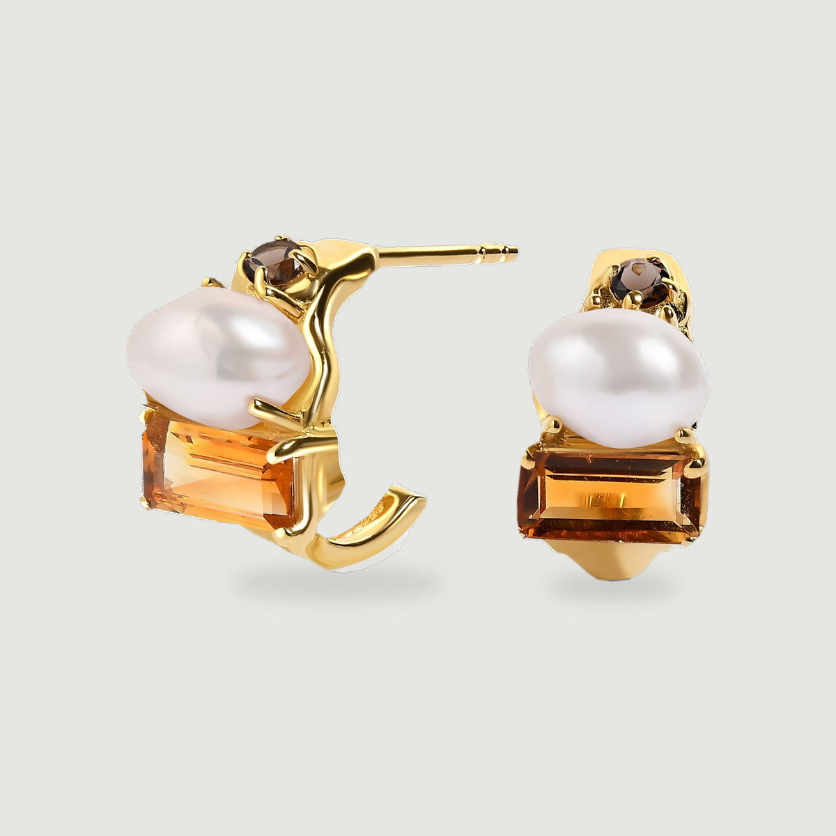 A pair of yellow gold open hoop earrings displays white pearls, rectangular amber-colored citrine and small round brown stones on a light gray surface.