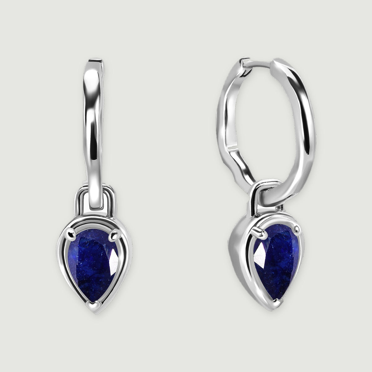 A pair of silver-tone hoops with deep blue pear-shaped sapphire drops rests on a light gray surface.