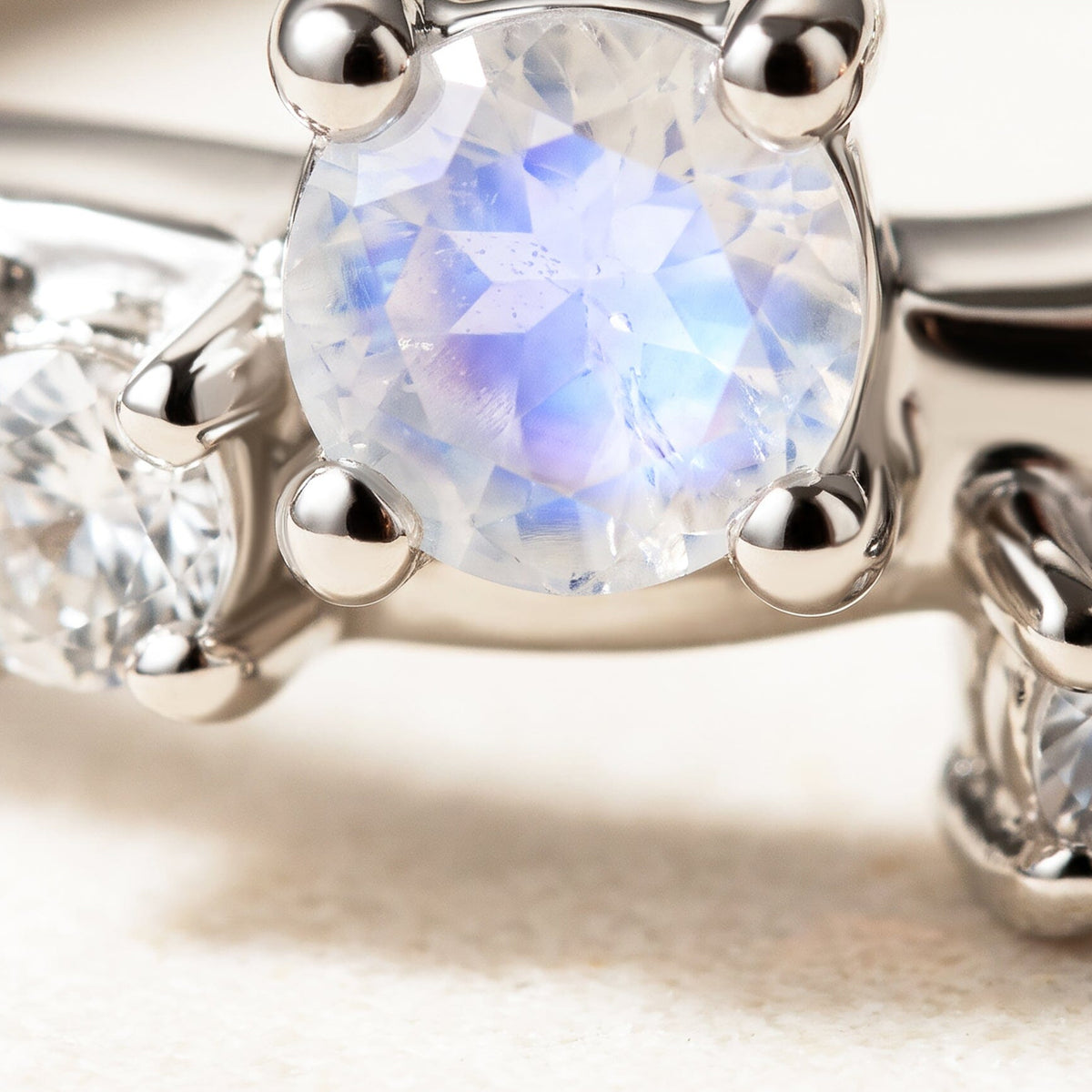 A close view shows blue flashes in a faceted moonstone held by silver prongs beside clear stones.