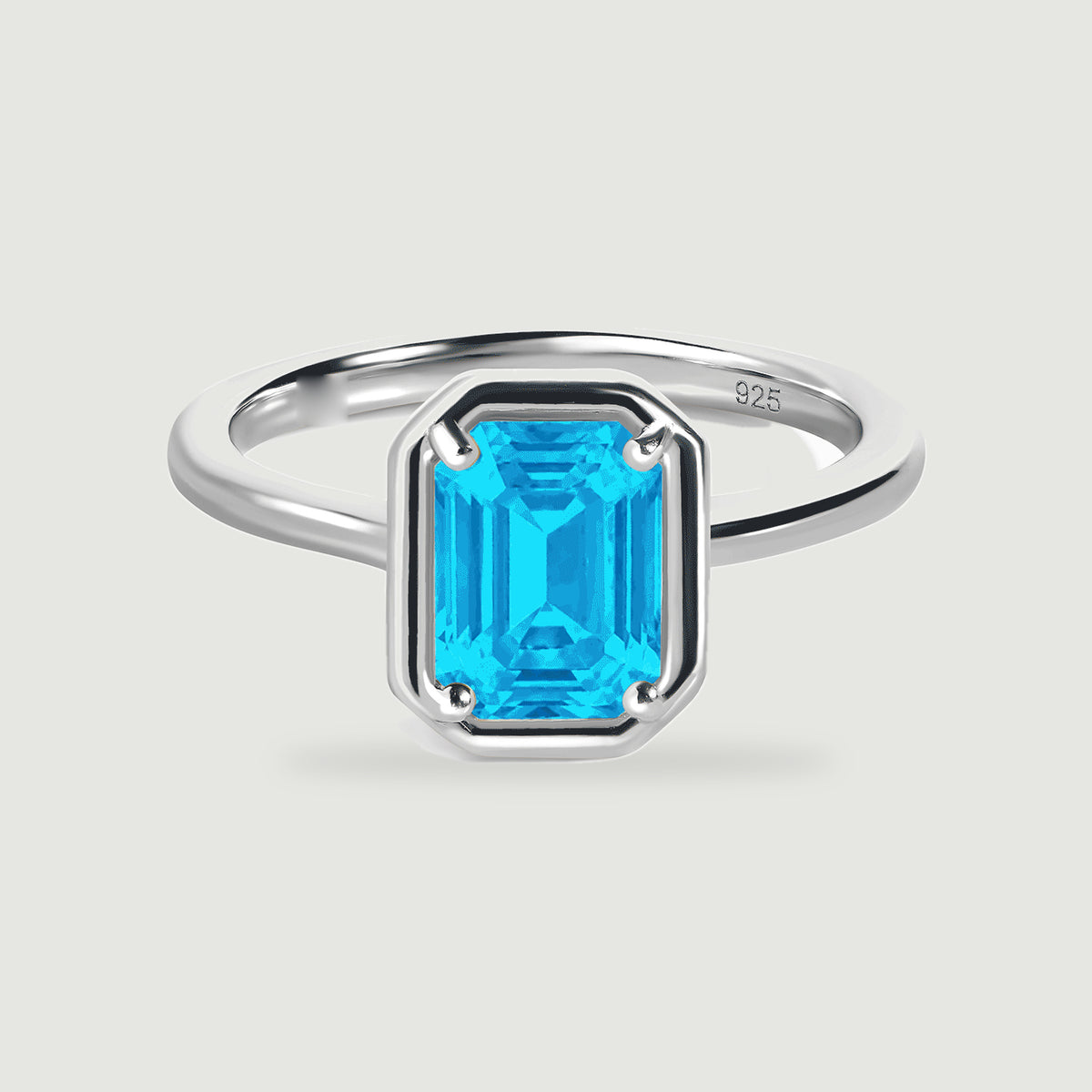 A polished silver ring with a bright blue rectangular stone sits centered on a pale grey surface.