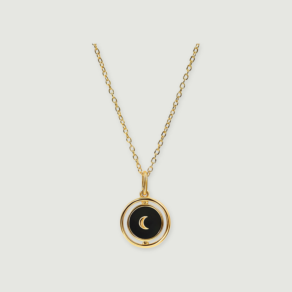 A yellow gold vermeil chain holds a round black onyx pendant with a gold crescent and a rotating outer frame.