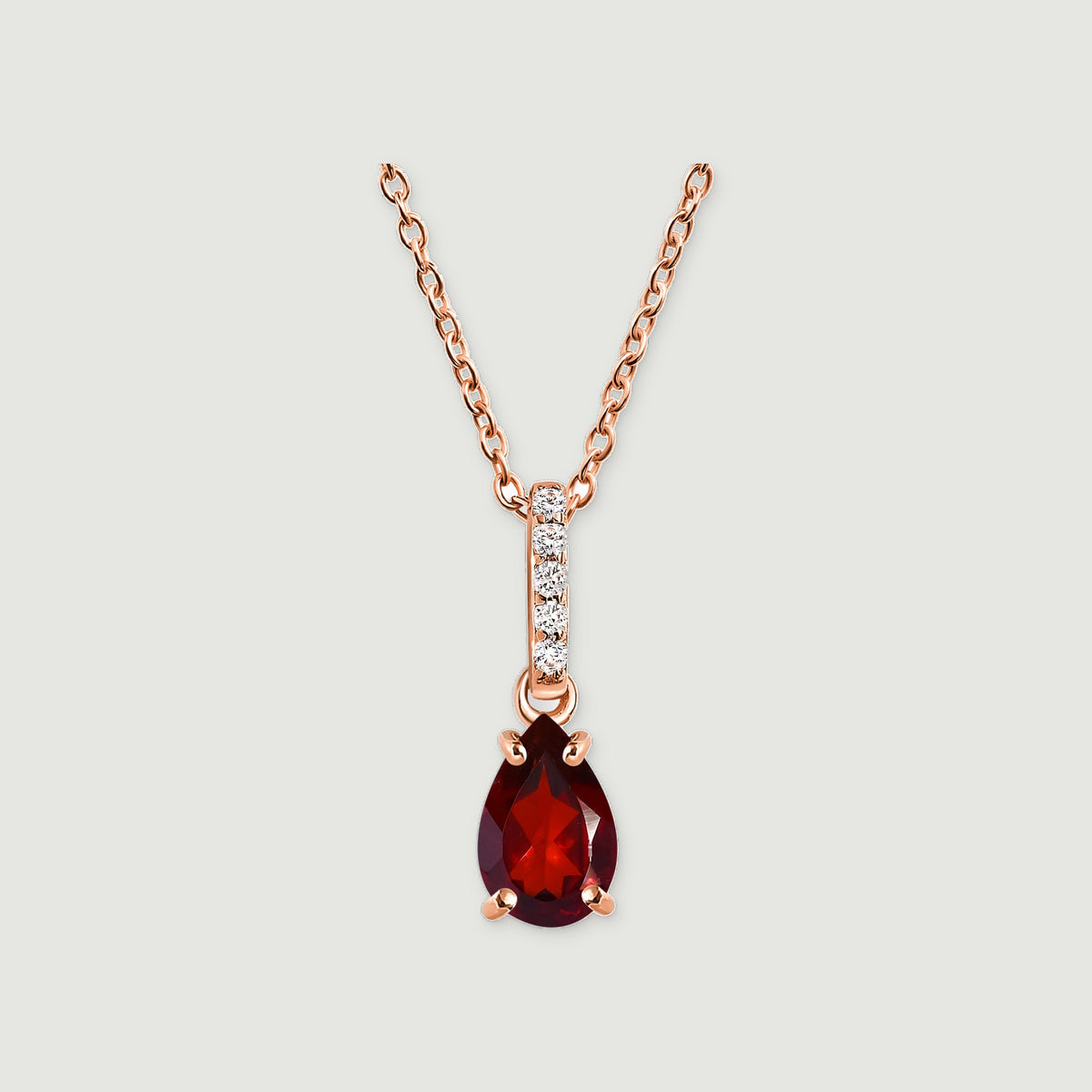 A rose gold necklace displays a faceted red drop and a diamond-set bail against a pale gray surface.