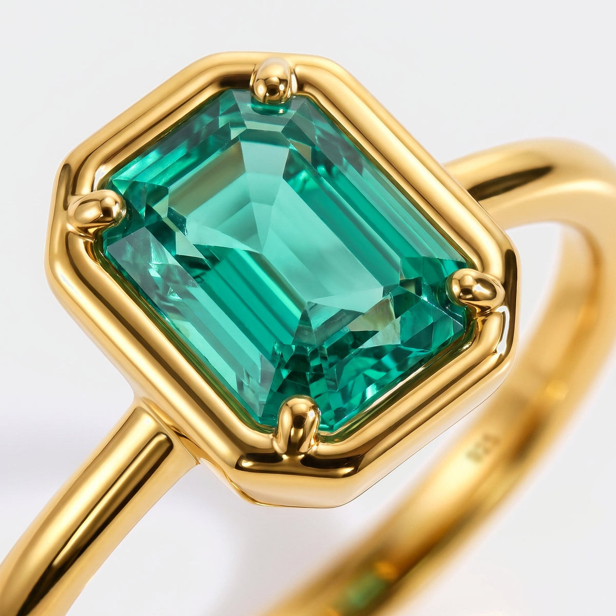 Green facets sit inside a polished yellow gold setting with rounded corner prongs.