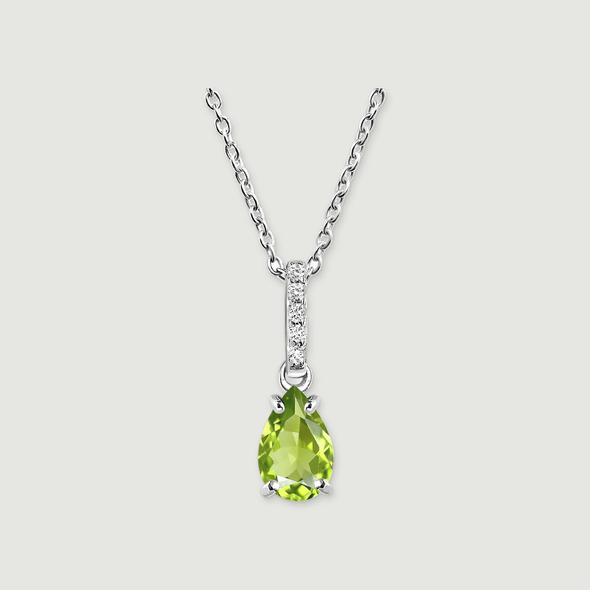 A silver chain meets a narrow white-stone bail above a faceted green pear pendant on a softly shadowed gray background.