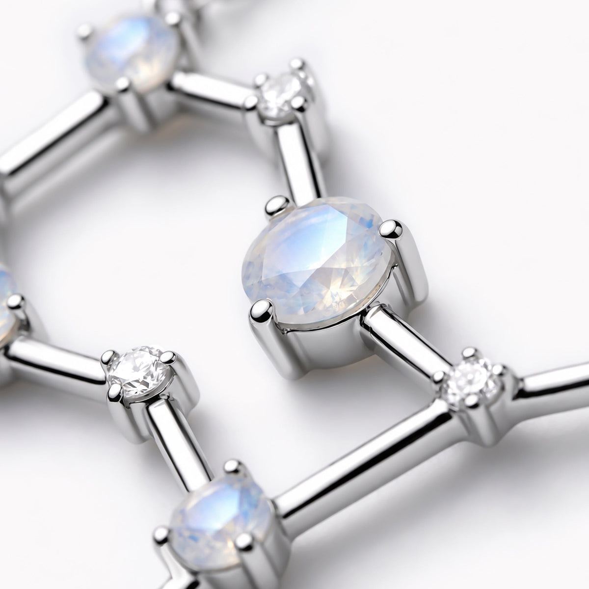 A faceted pale blue moonstone sits in a silver prong setting between polished bars and small round clear stones.
