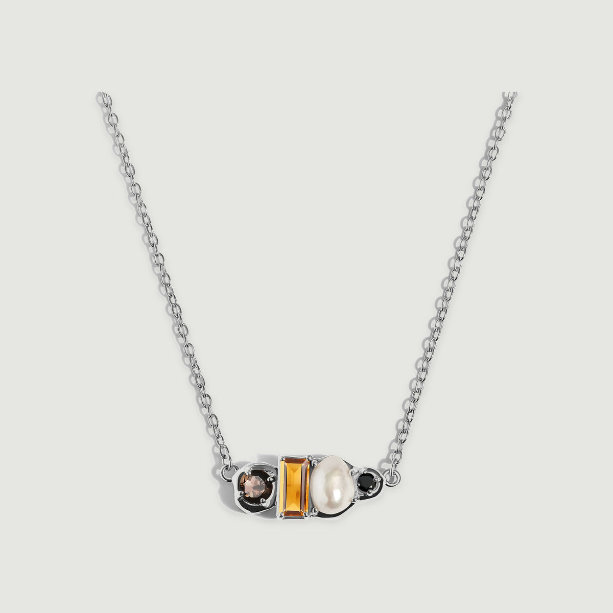 A sterling silver necklace shows a rectangular amber citrine, an oval pearl and two round dark stones between fine cable chains.