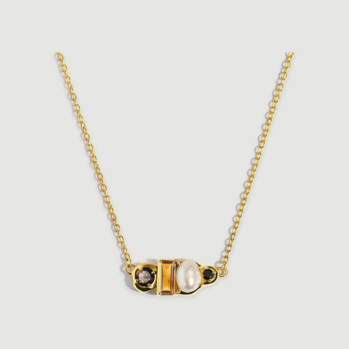 A yellow gold vermeil necklace presents a horizontal cluster of faceted amber citrine, a cream pearl and round dark gemstones.