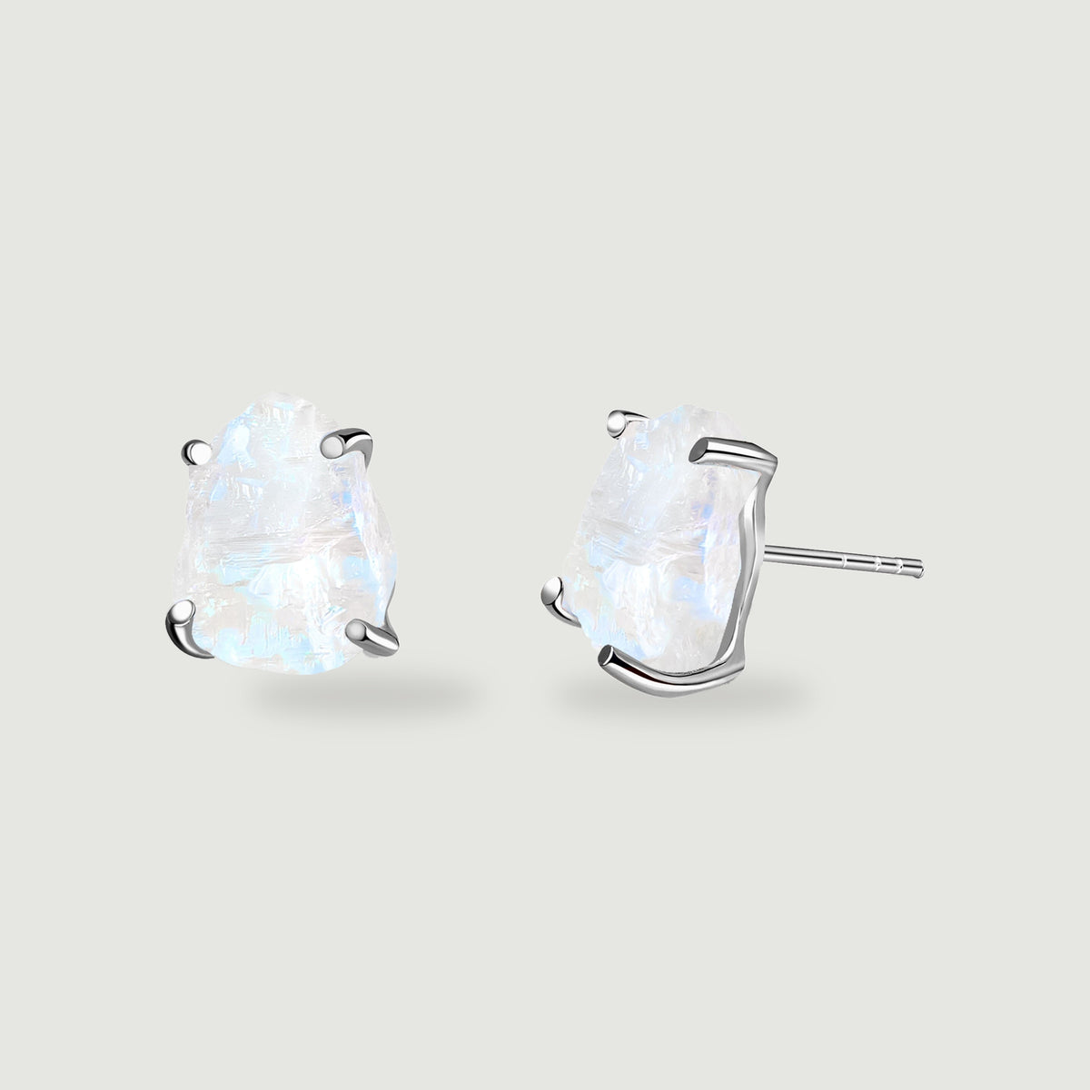Two raw moonstone studs with silver prongs rest on a light gray surface, with one post visible.