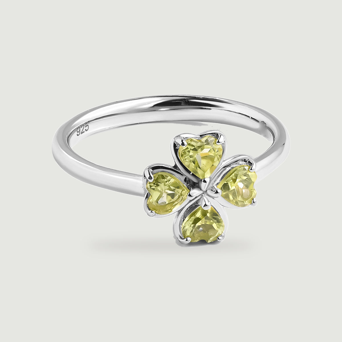A sterling silver ring with a four-leaf green peridot setting rests on a soft gray background.