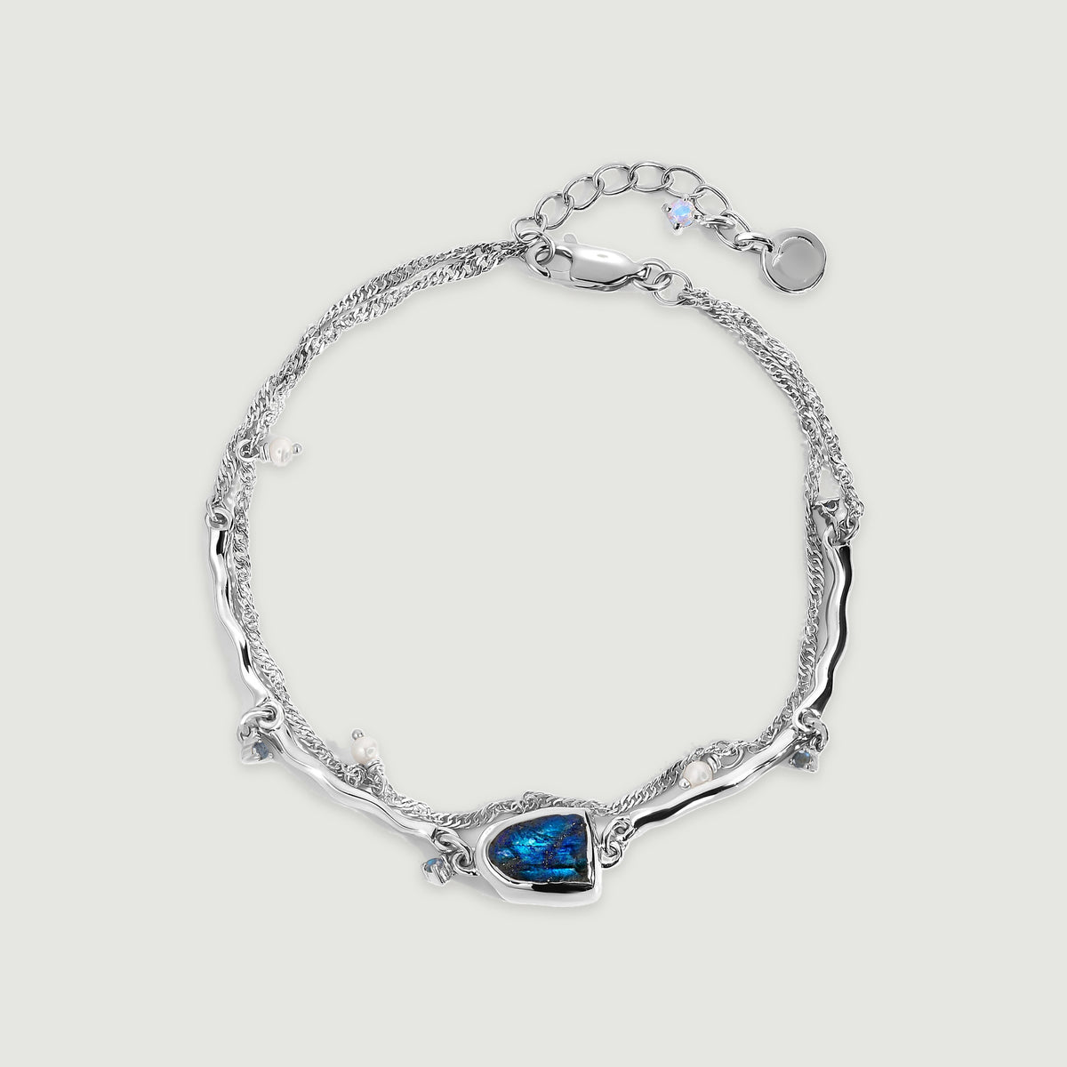 A sterling silver bracelet forms an oval around an open center, with a blue labradorite setting and small pearl charms on a pale gray background.