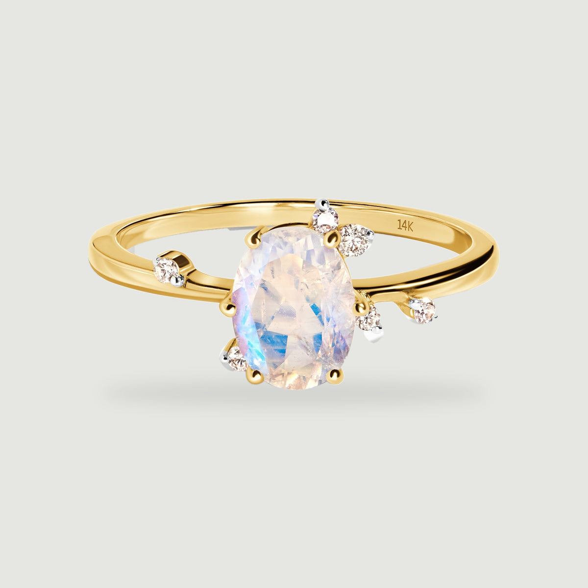 A yellow gold ring displays an oval faceted moonstone and scattered round diamond accents on a light gray background.