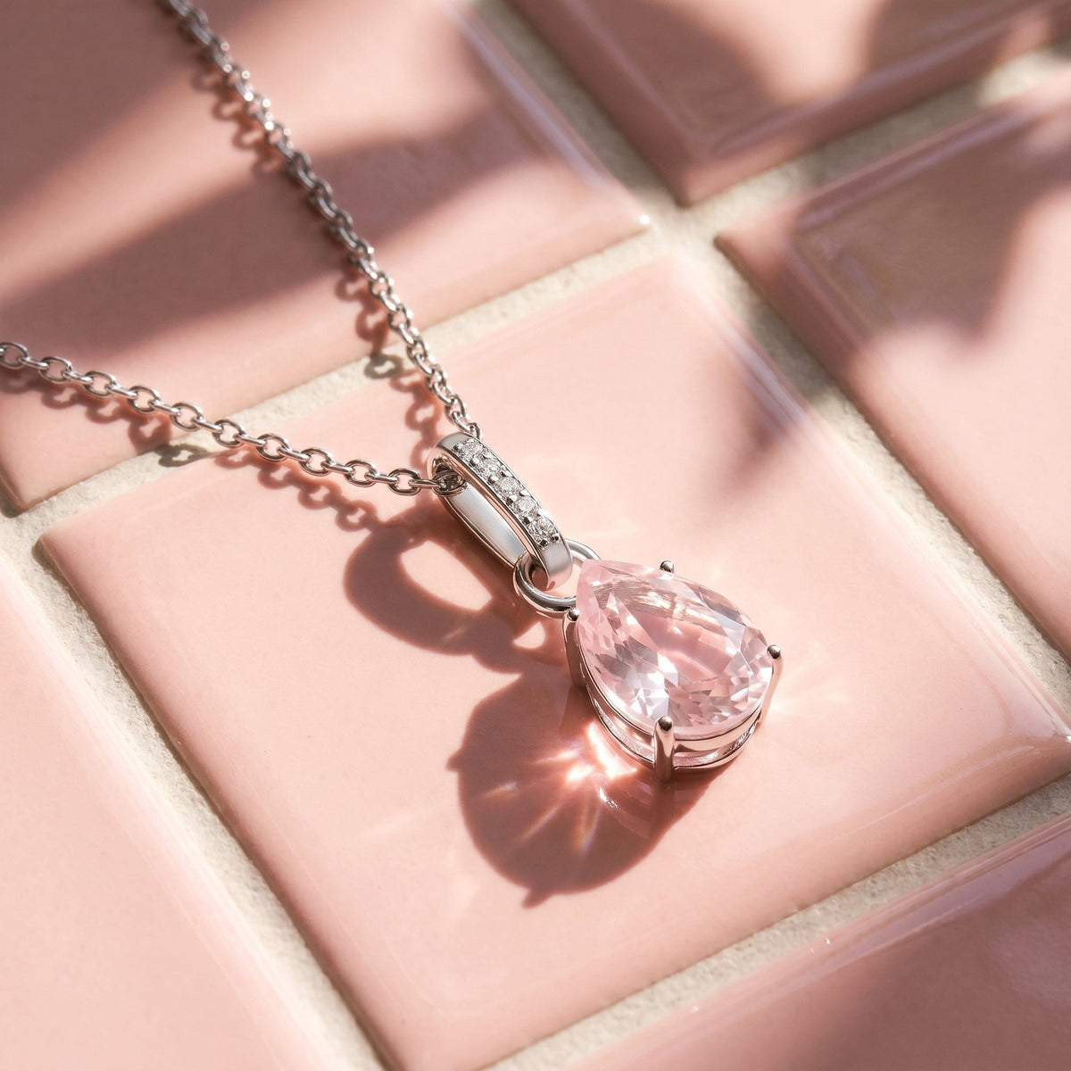 Sunlight casts the shadow of a silver rose quartz pendant and its chain across a pink tiled surface.