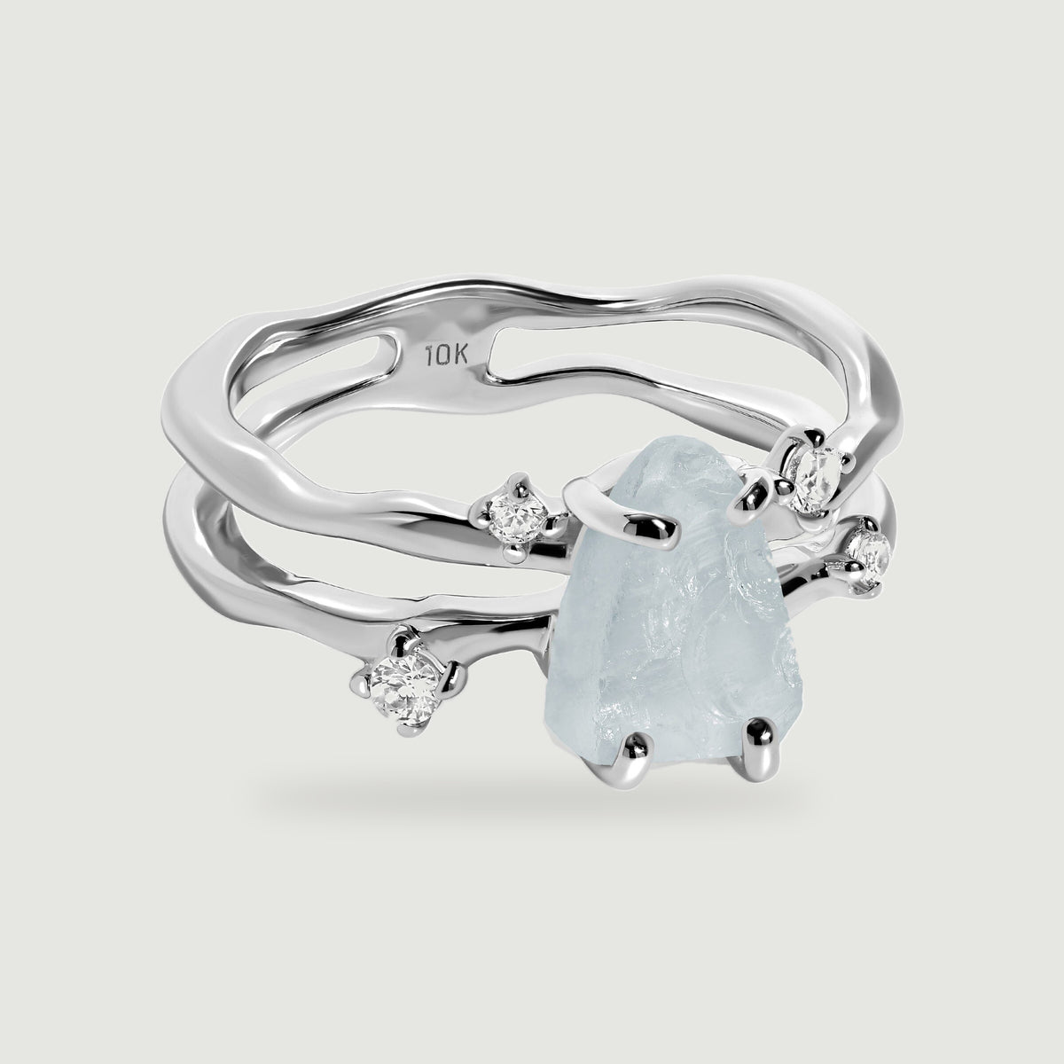 A white gold ring displays a raw aquamarine held by polished prongs beside four clear accent stones.