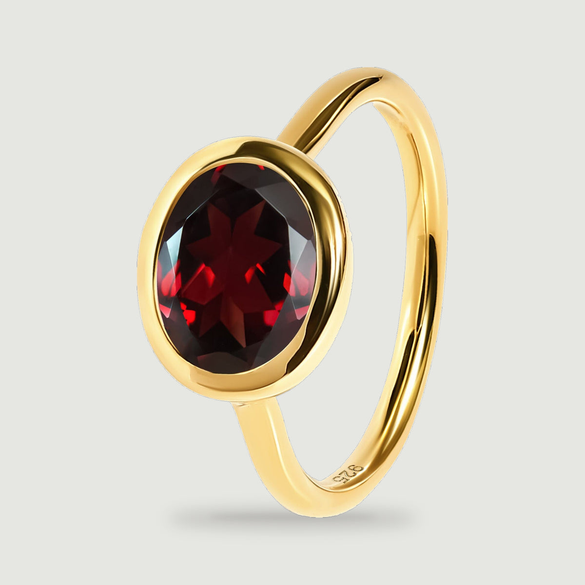 The yellow gold ring stands at an upright angle, showing its slim band and oval garnet setting.