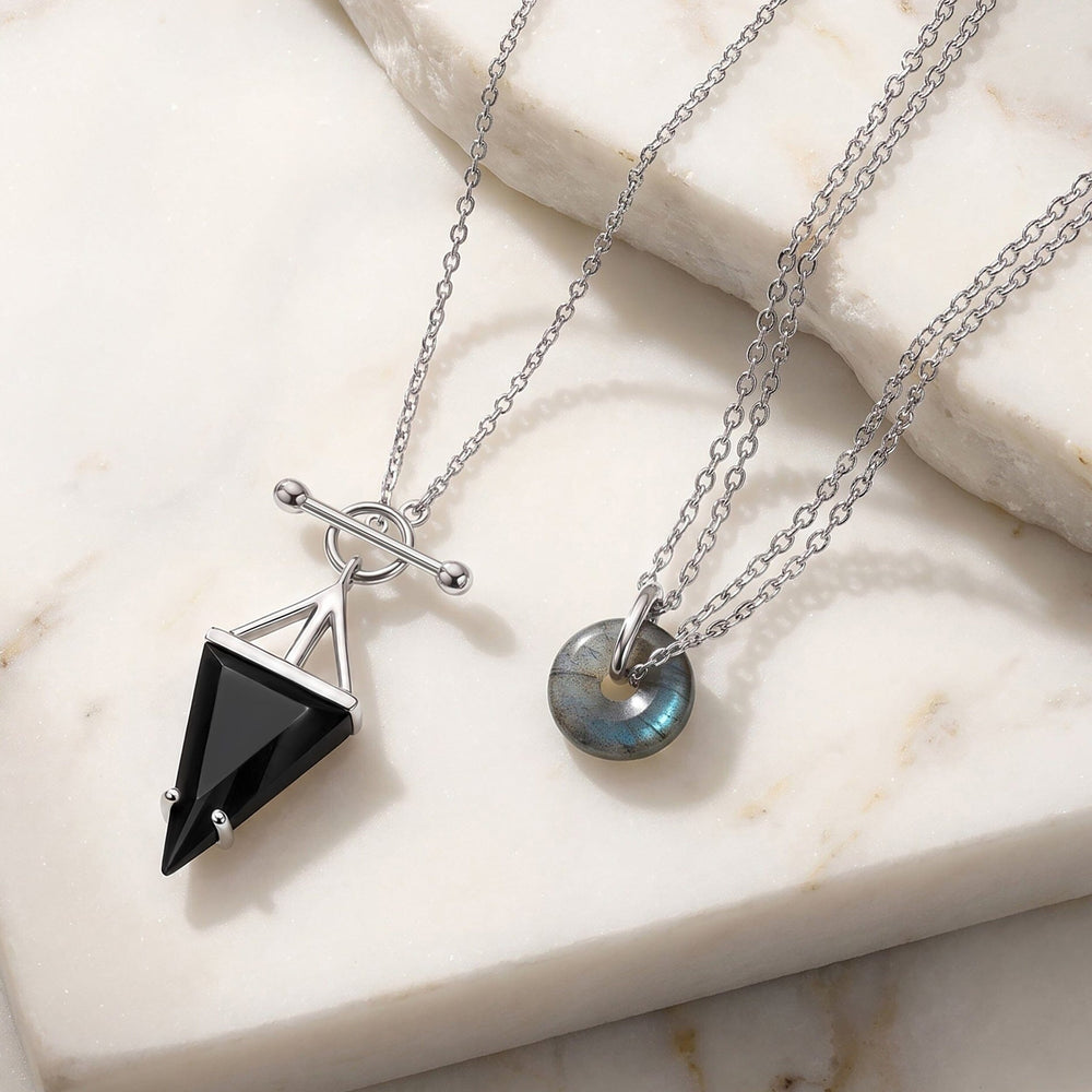 Silver necklaces on a marble surface with a black obsidian pendant and a labradorite donut