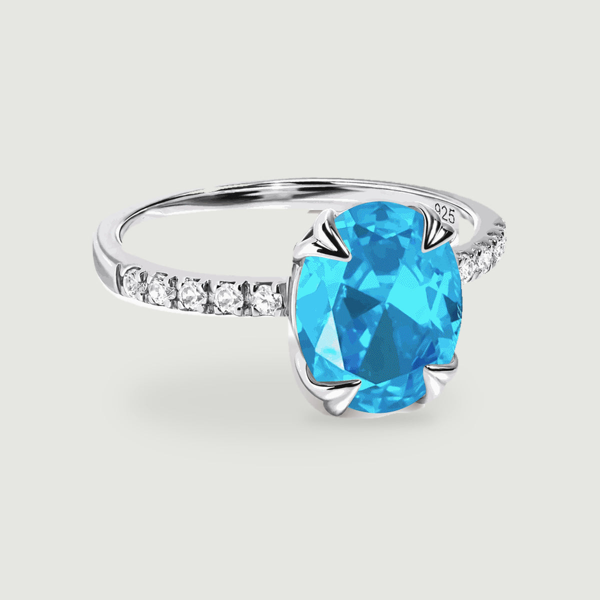 A sterling silver ring with an oval blue gemstone and clear stones along the band rests on a light grey surface.