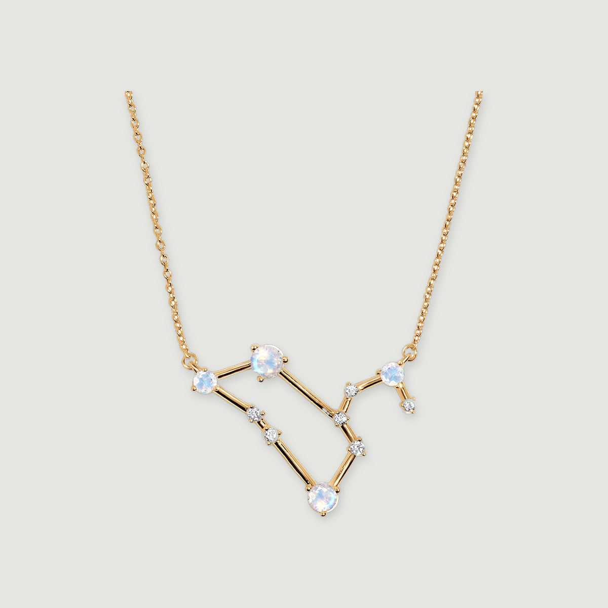 A yellow gold necklace with four pale moonstones and small clear stones rests on a light gray background.