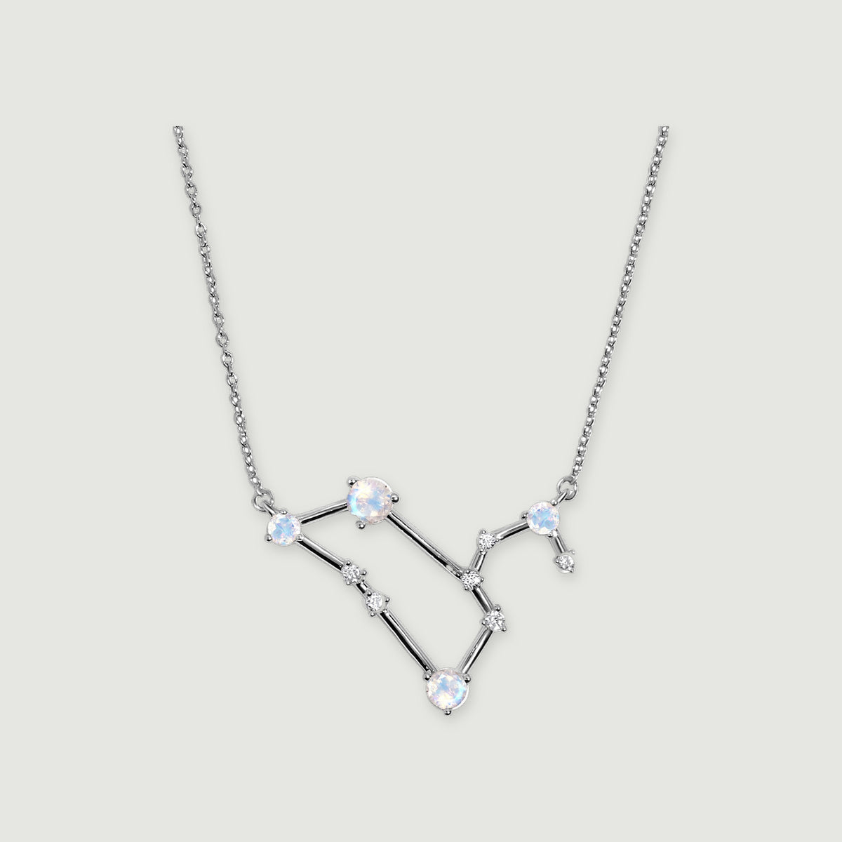 A silver chain frames a geometric pendant with round moonstones and clear accents against light gray.