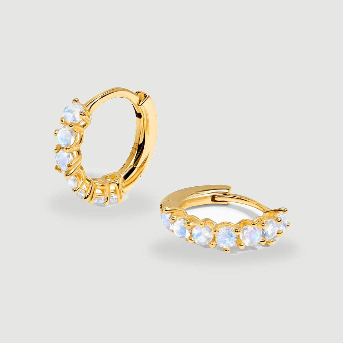 A pair of yellow gold moonstone hoops shows round pale stones and hinged closures.