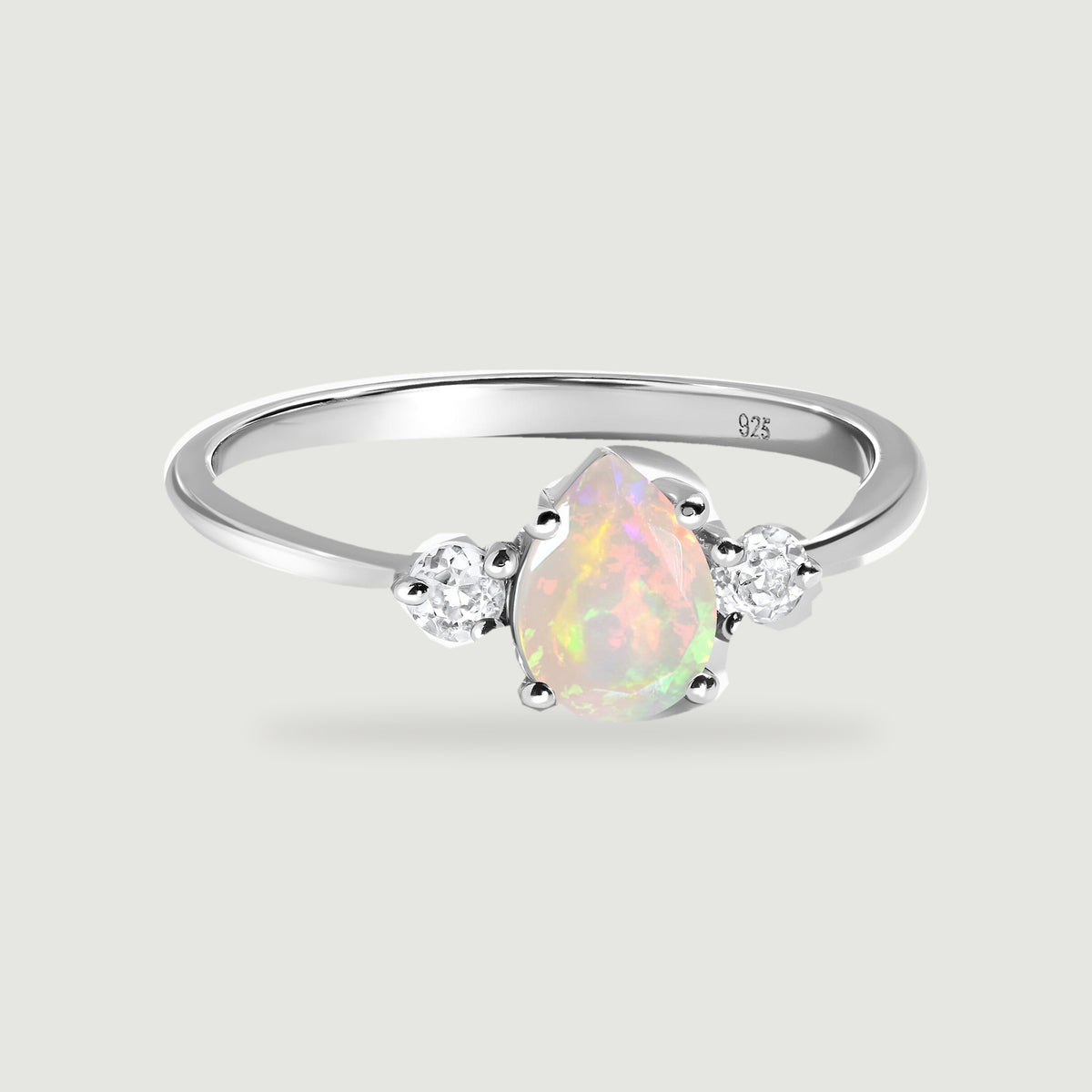 A polished silver ring surrounds a pear-shaped opal with two round clear side stones.