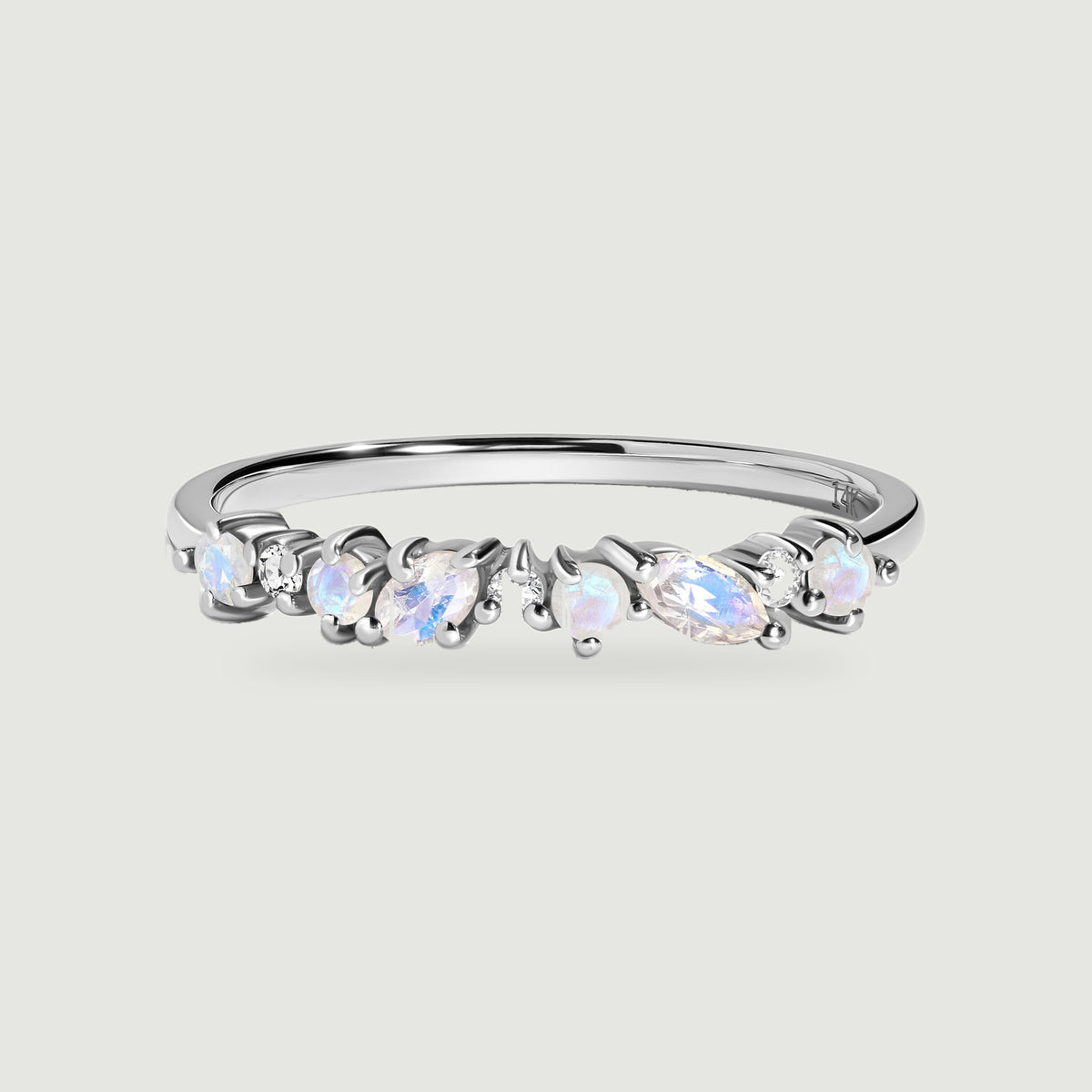 A white gold ring is centered on a light gray surface with a row of blue flashing moonstones and clear diamonds.