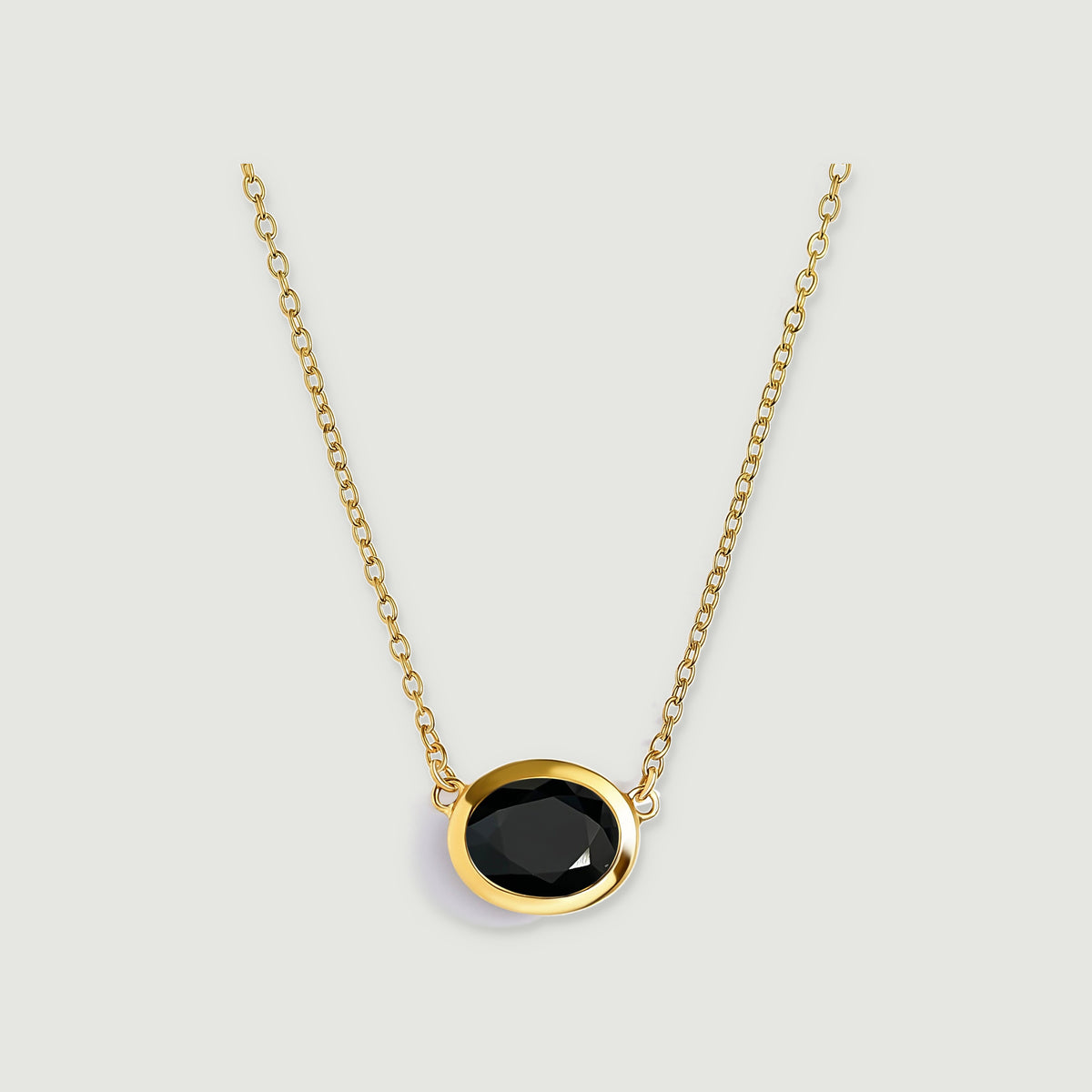 A yellow-gold-plated chain holds a faceted oval black obsidian pendant against a light grey background.