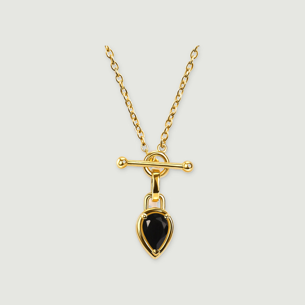 A yellow gold plated necklace has an oval-link chain, a horizontal bar clasp, and a pear-shaped black stone on a light grey background.