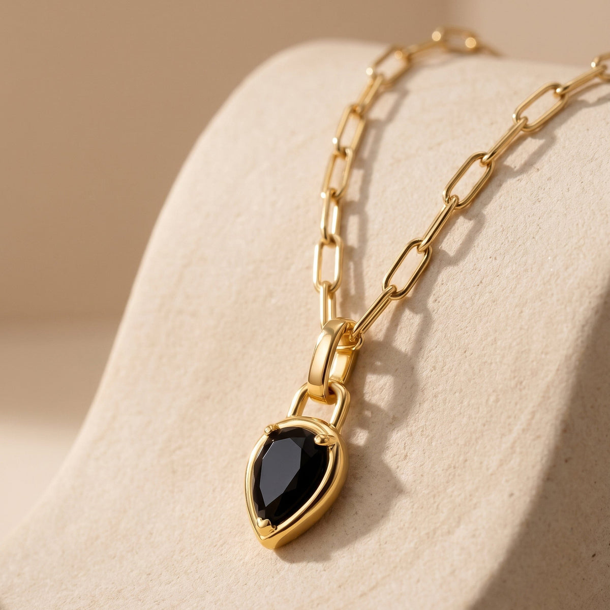 A gold-tone necklace lies diagonally across a textured cream stone surface.