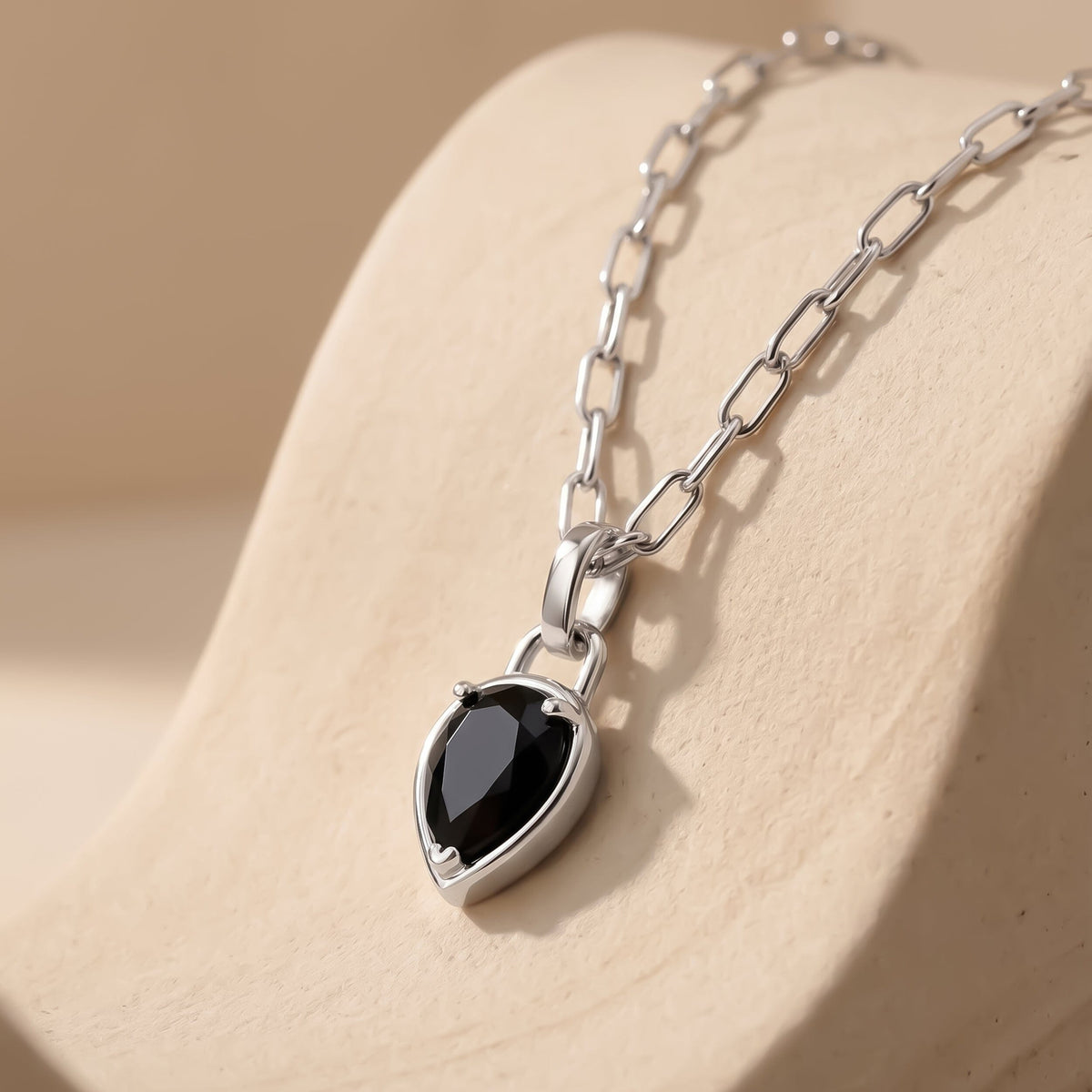 A rhodium plated necklace rests on pale stone with its black pendant pointing downward.