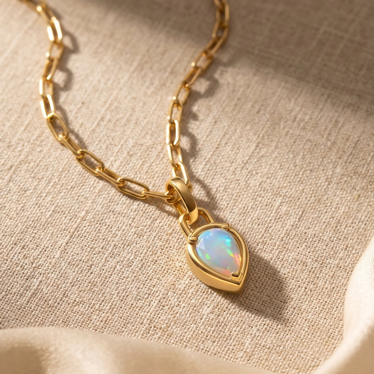 The yellow gold opal necklace rests diagonally on textured beige fabric in warm light.
