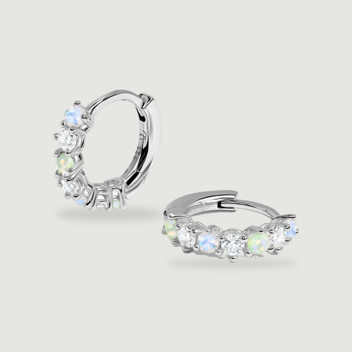 A pair of sterling silver gemstone hoops is centered on a pale grey surface with soft shadows.