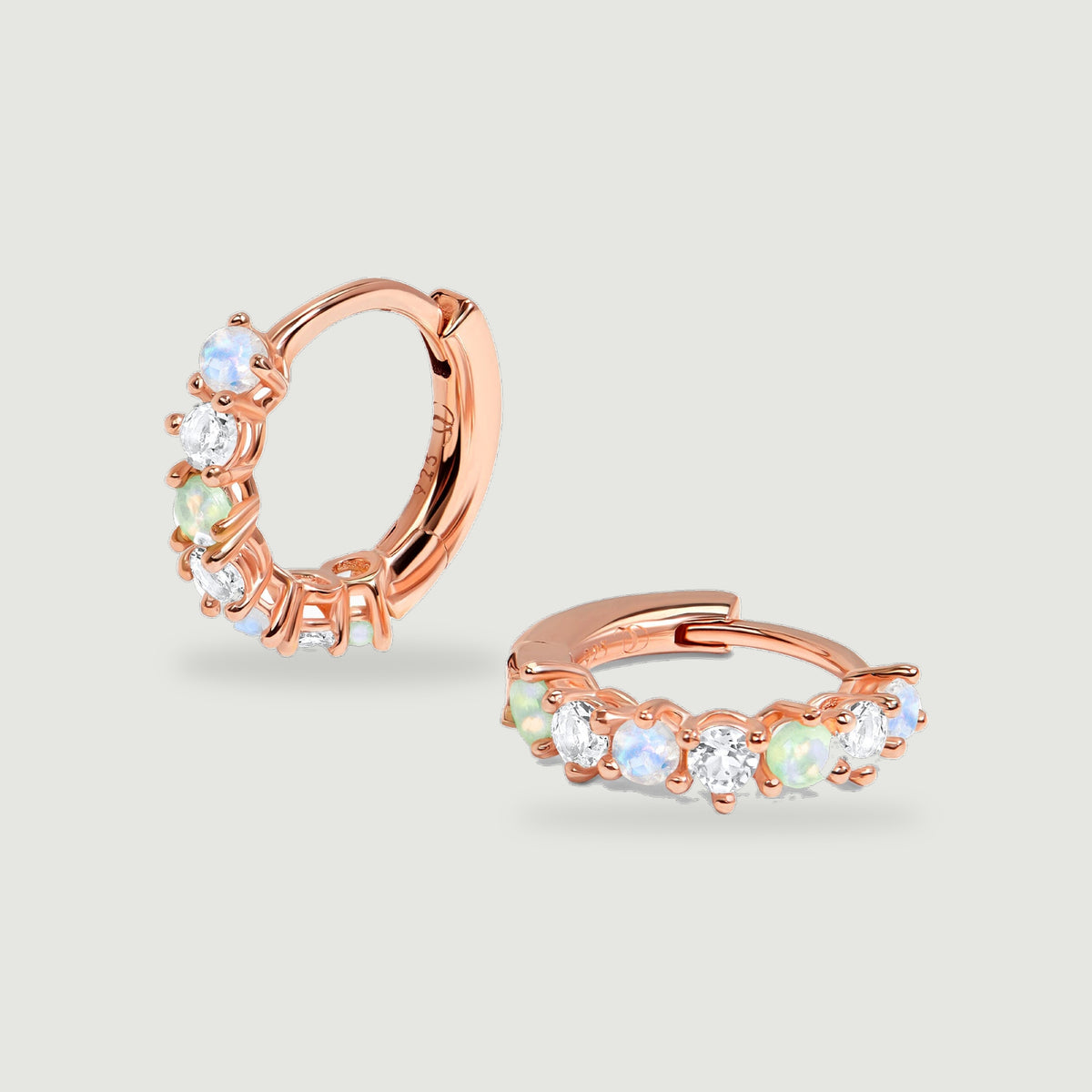 Rose gold vermeil hoop earrings rest together on a grey background with their prong settings visible.