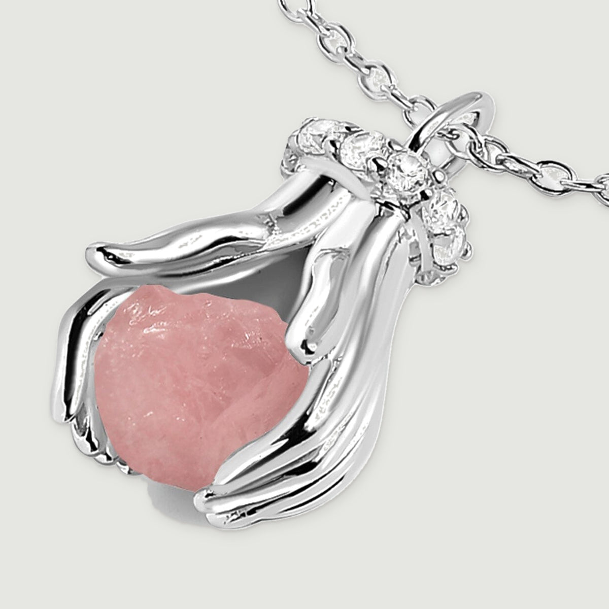 A silver pendant lies at an angle, revealing the uneven pink stone, polished fingers, and clear accents beside the chain.