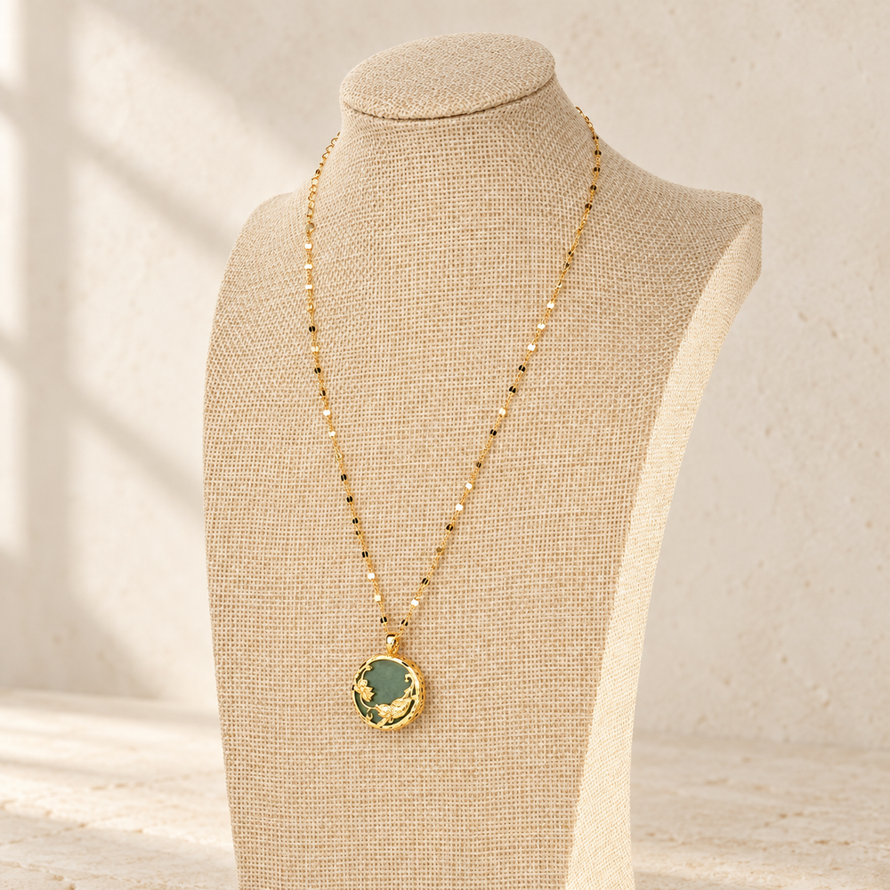 Green koi and lotus pendant displayed on a linen necklace stand.