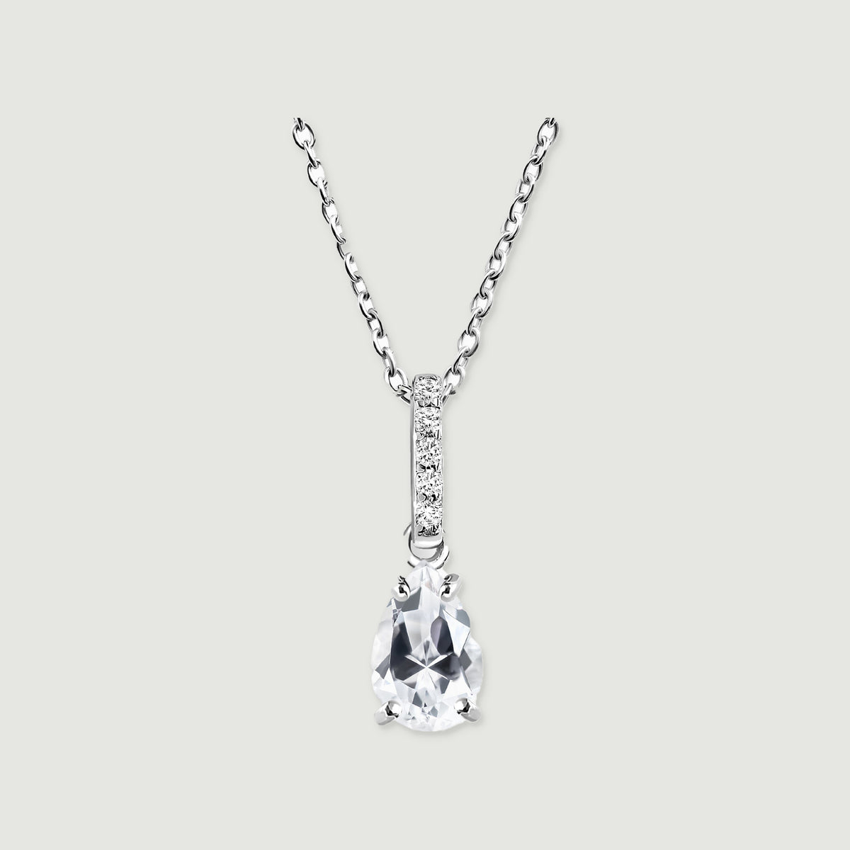 A sterling silver necklace with a clear pear-shaped pendant and a stone-set bail rests on a light gray background.