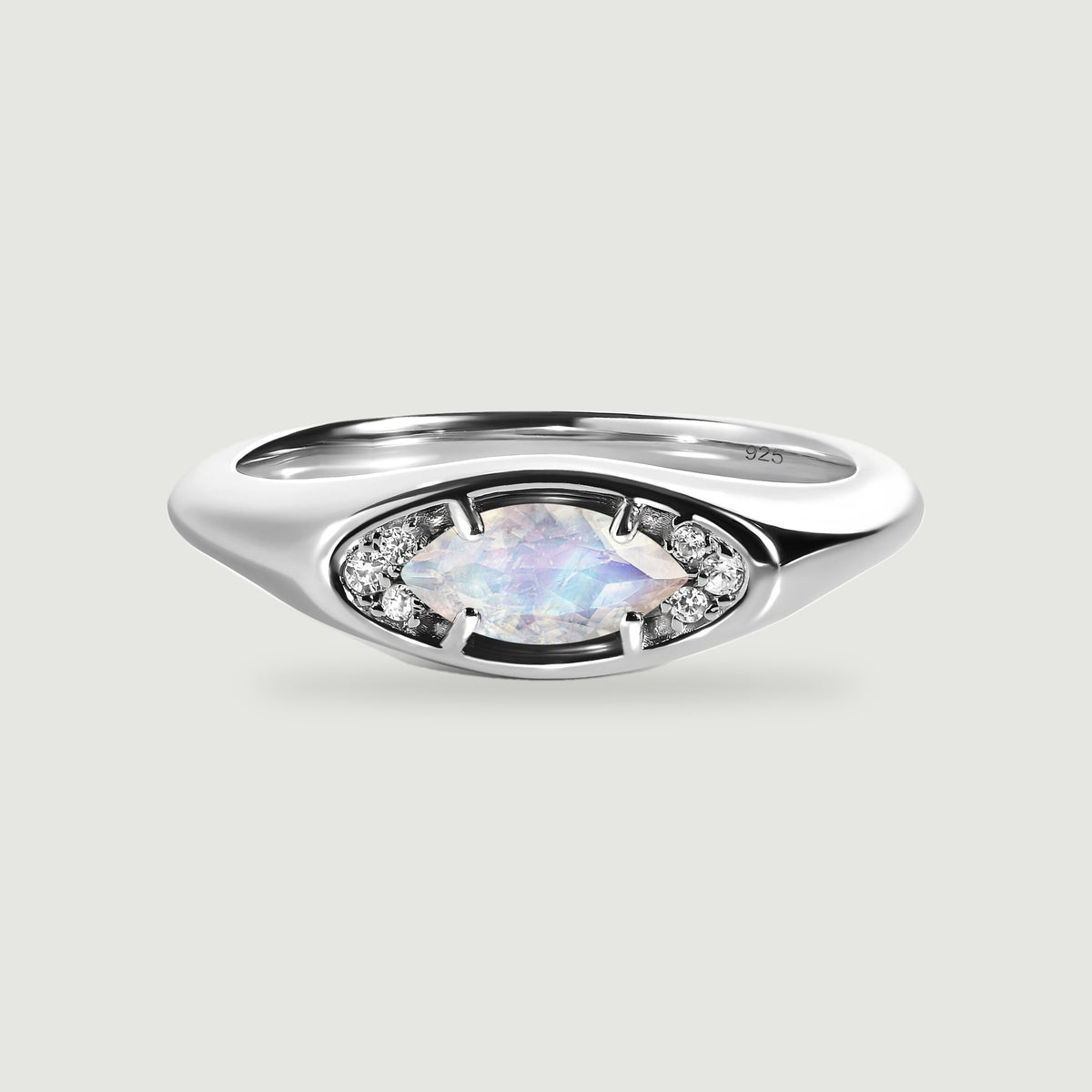 A polished silver ring frames a pale faceted moonstone between two clusters of small clear stones.